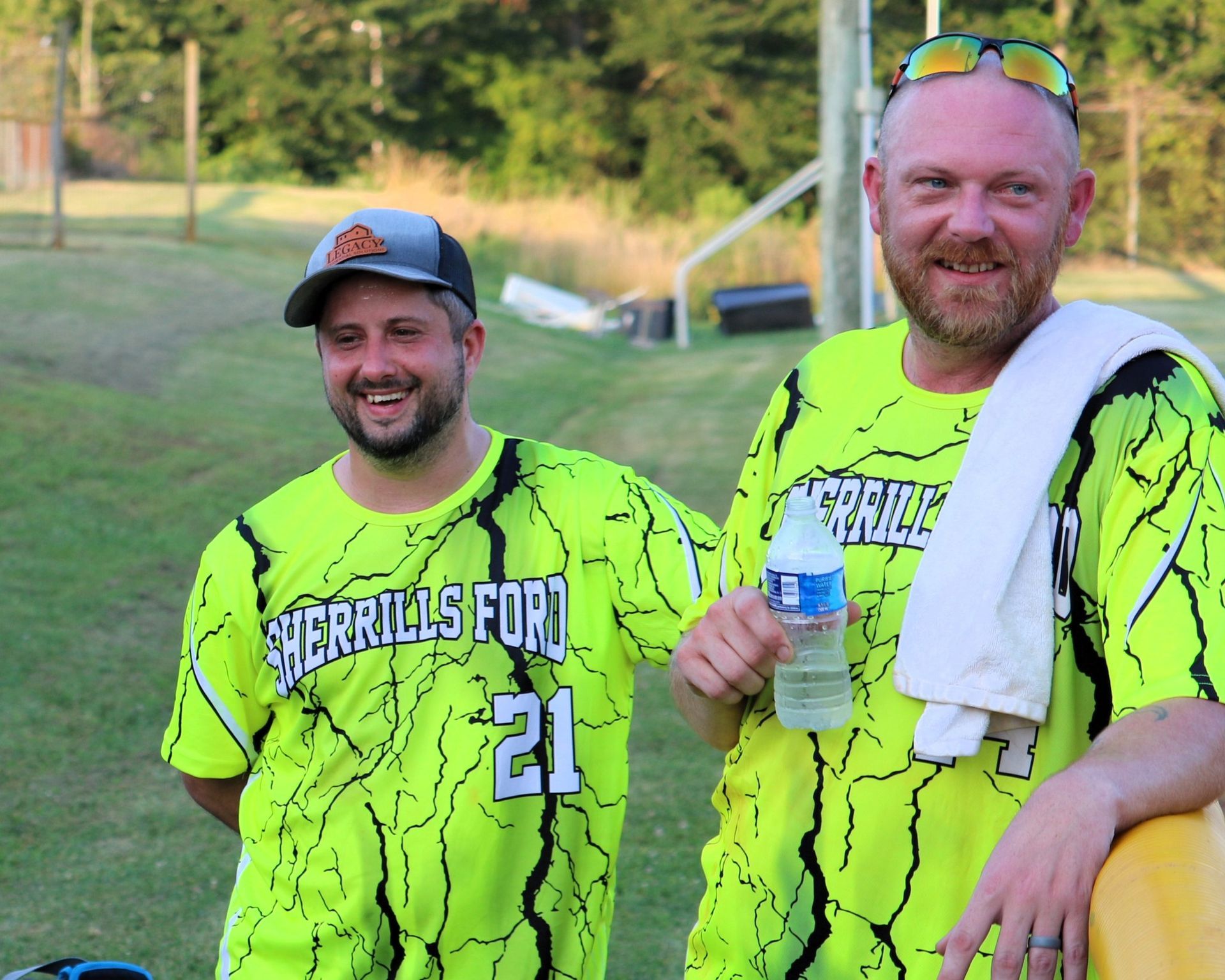 Two men in neon shirts with "Burrito Score" text smiling outdoors. One holds water bottle.