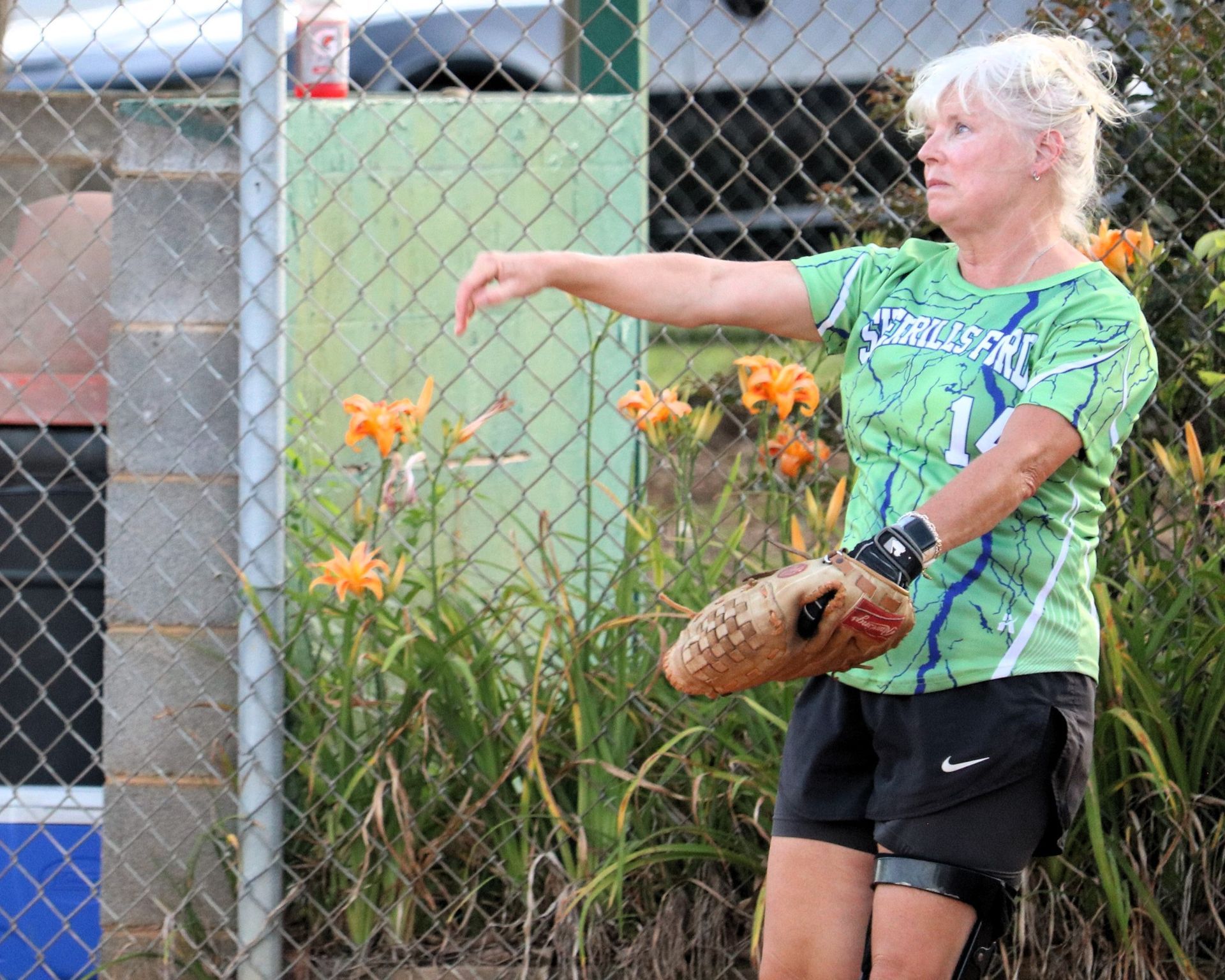 Woman in softball gear, holding a mitt, arm extended, on a field.
