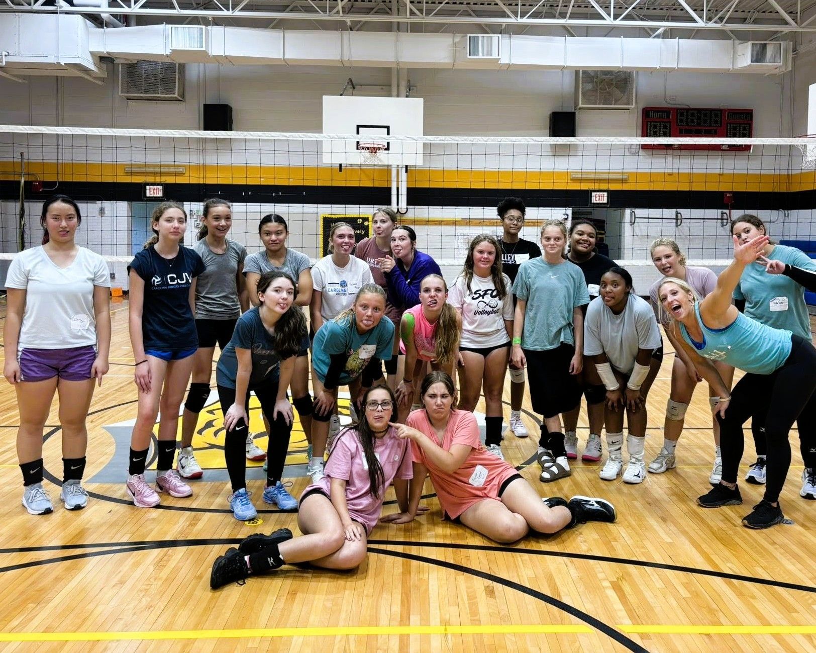 Group of volleyball players posing on a court with smiles, in casual athletic wear.