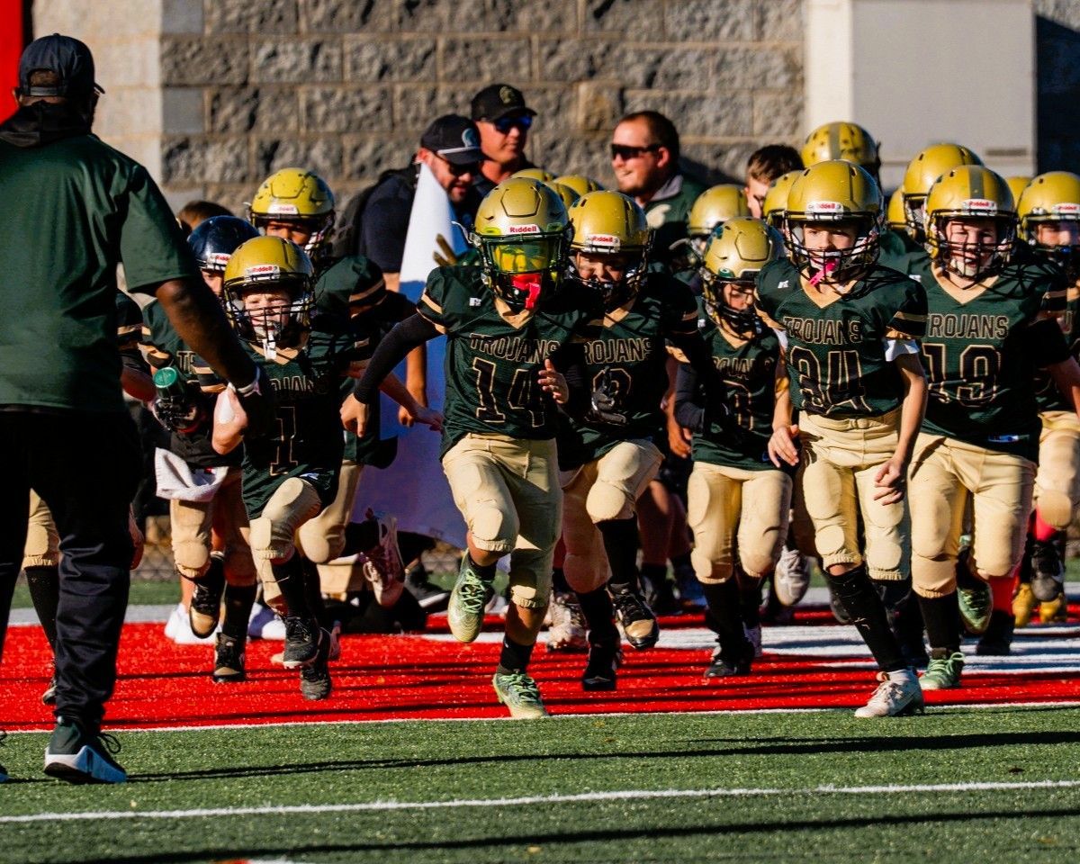 Youth football team in gold and green uniforms runs onto a field.