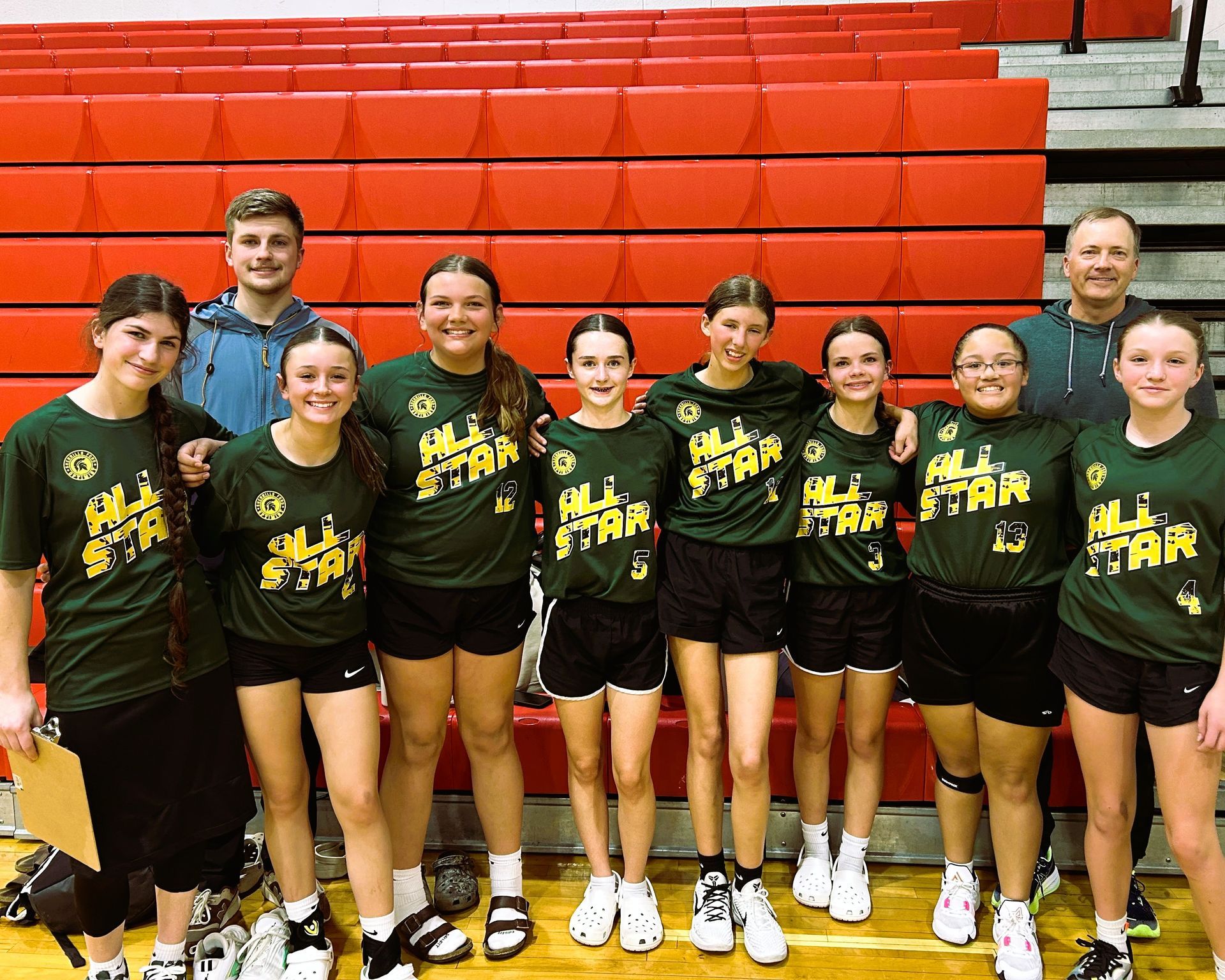 Volleyball team posing after a game. Green and gold jerseys in a gym with red walls.