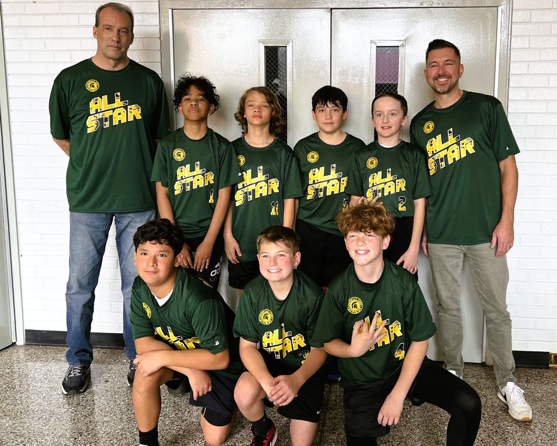 Group photo of a youth sports team wearing green shirts in front of a building.