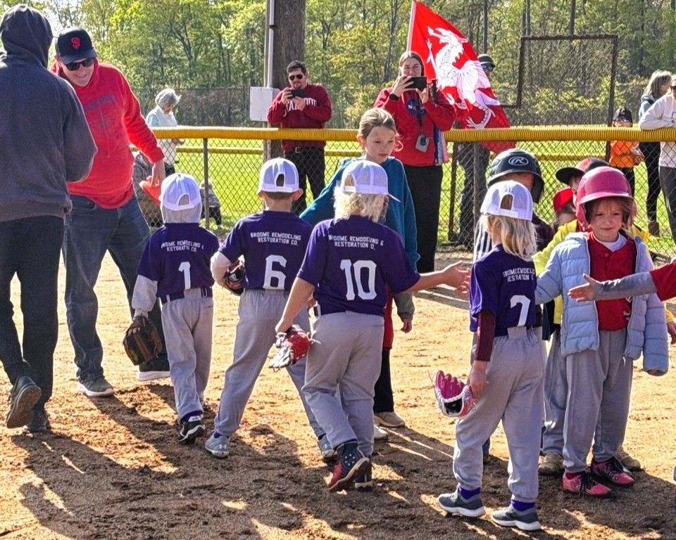 Youth baseball team in purple jerseys, leaving the field, being greeted by adults.