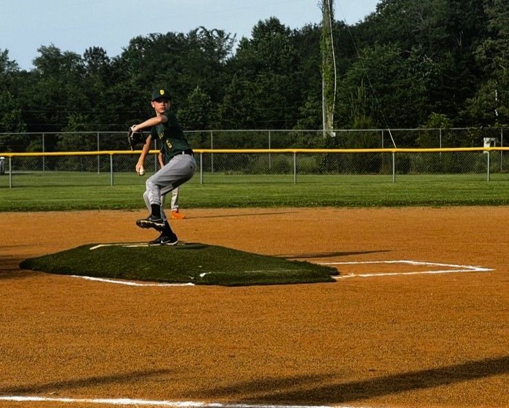 Baseball pitcher in green uniform throws a pitch from the mound on a baseball field.