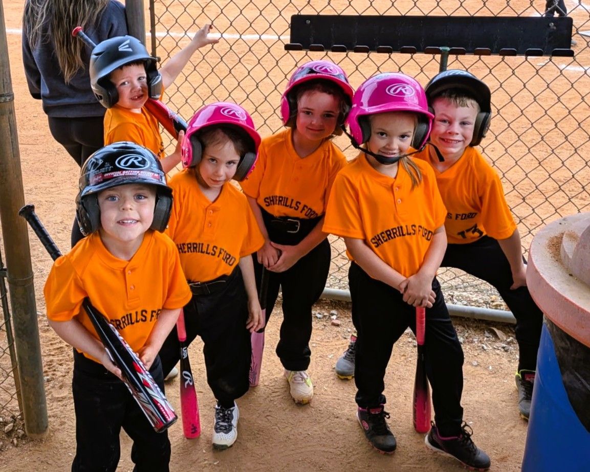 Youth softball team in orange jerseys and helmets posing near a fence, holding bats.