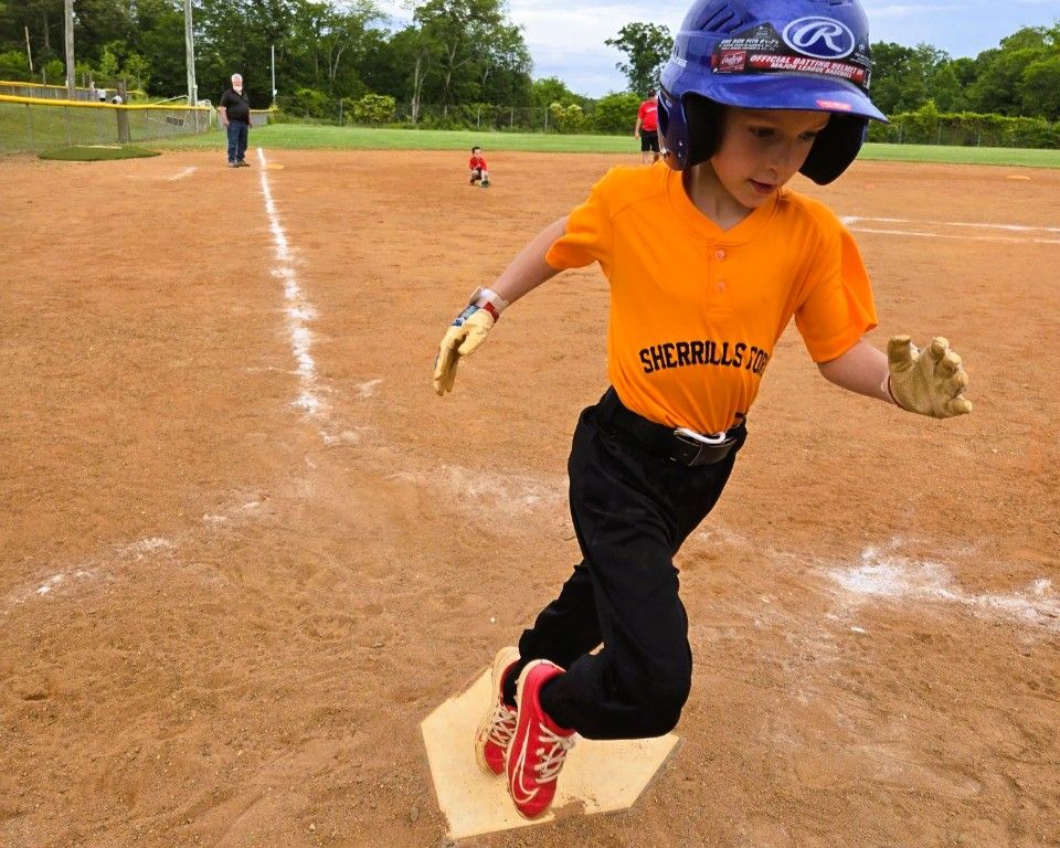 Boy in orange shirt and helmet slides into first base during a baseball game.
