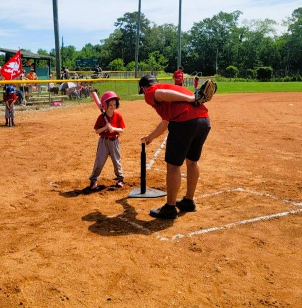 Boy in red helmet batting in baseball game, pitcher throwing ball.