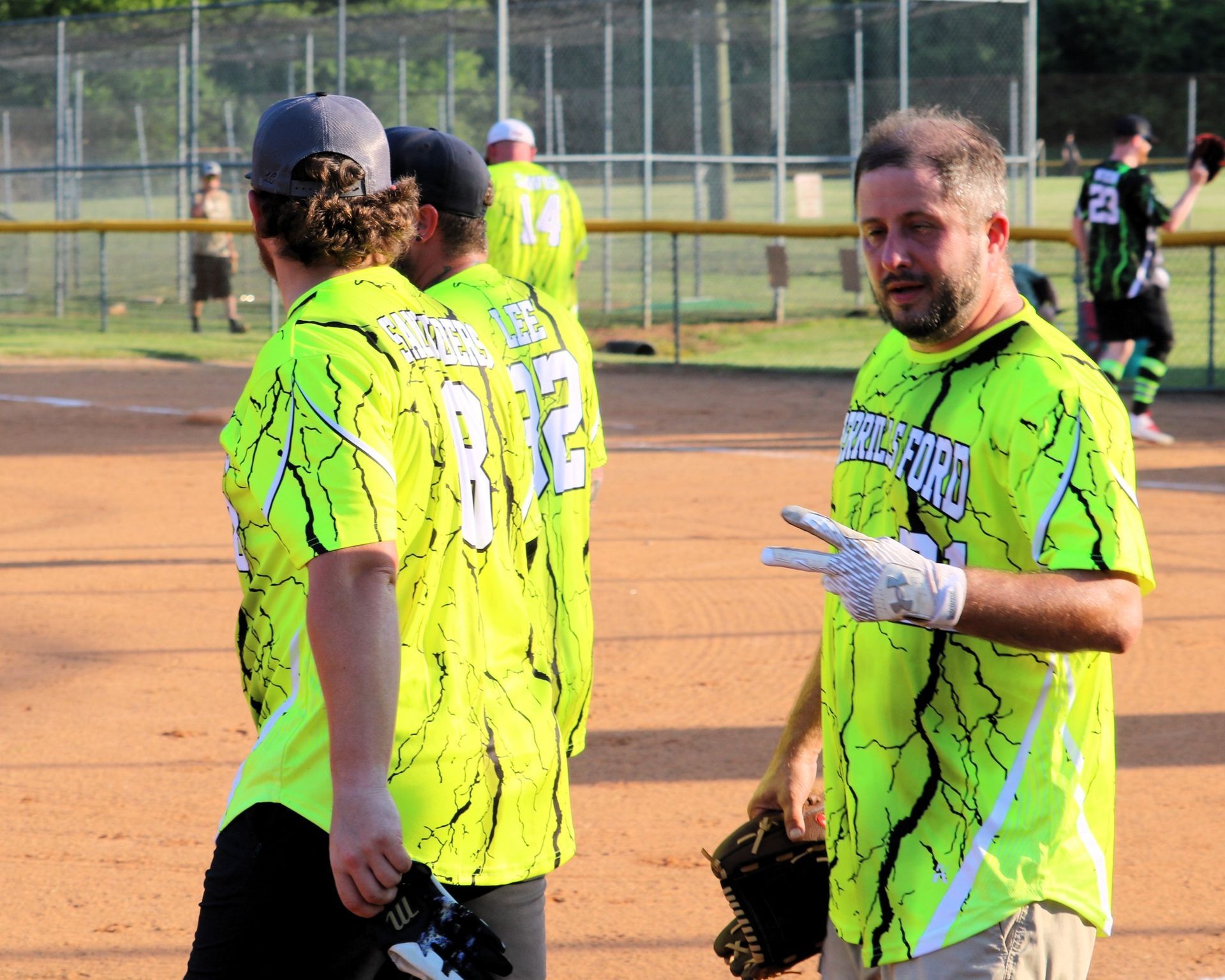 Softball players wearing neon jerseys on a field. One man makes a peace sign.