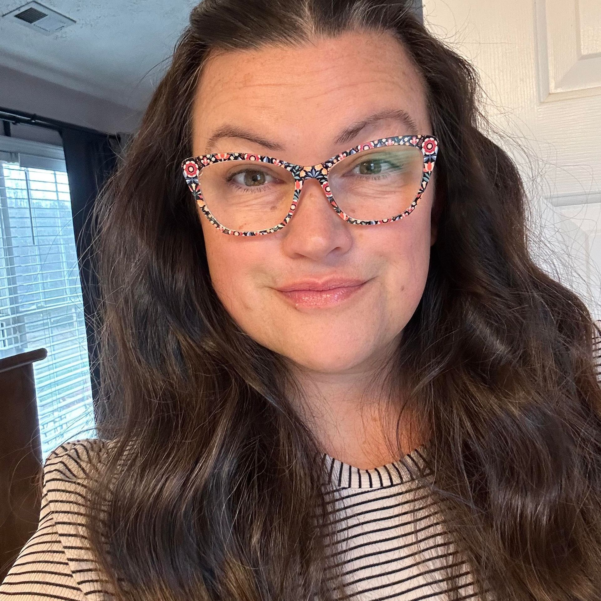 Woman with patterned glasses smiles, wearing a striped shirt.