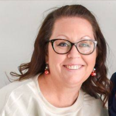 Woman with glasses smiles, wearing earrings.