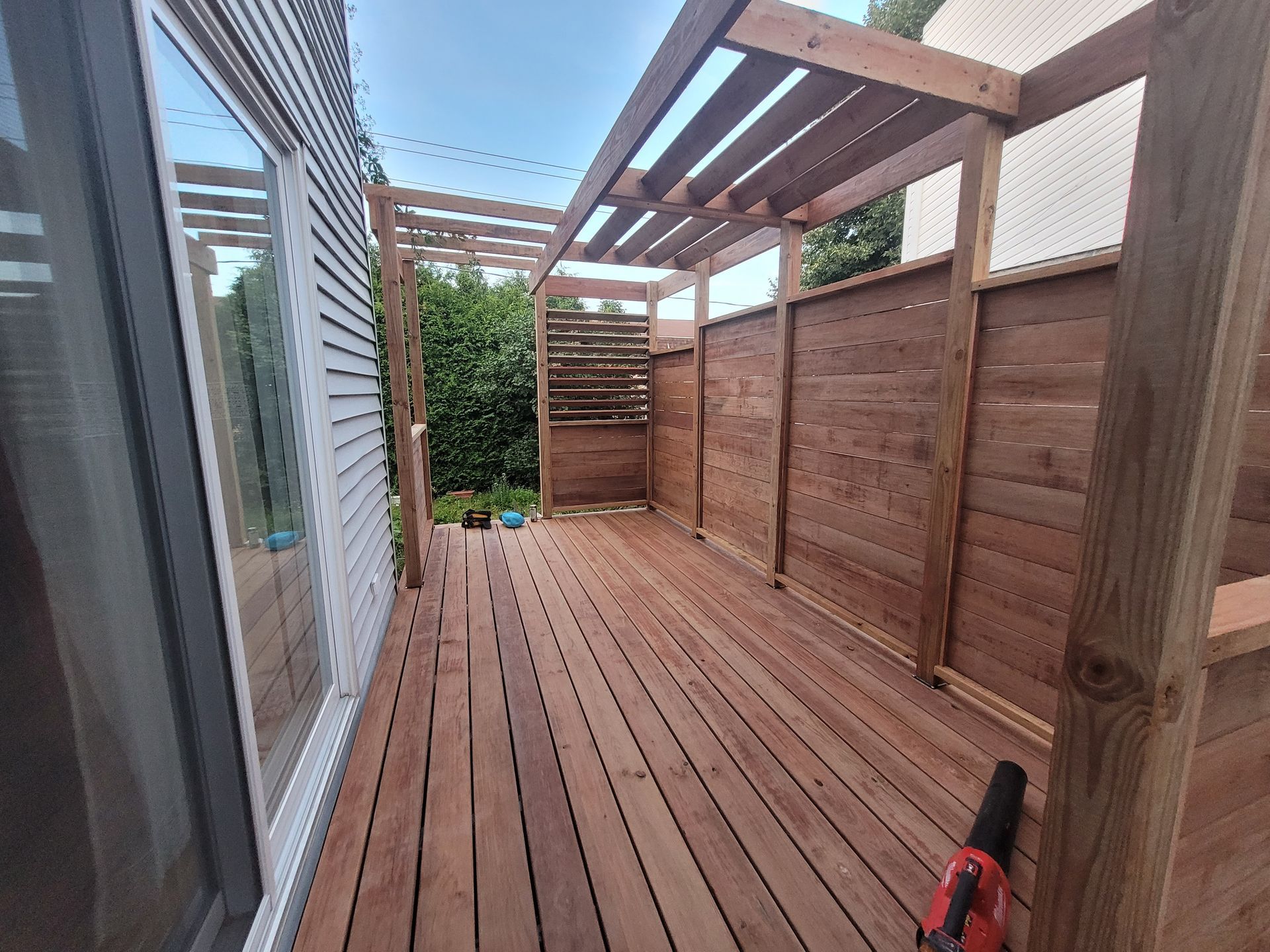 Une terrasse en bois avec une pergola et une clôture devant une maison.