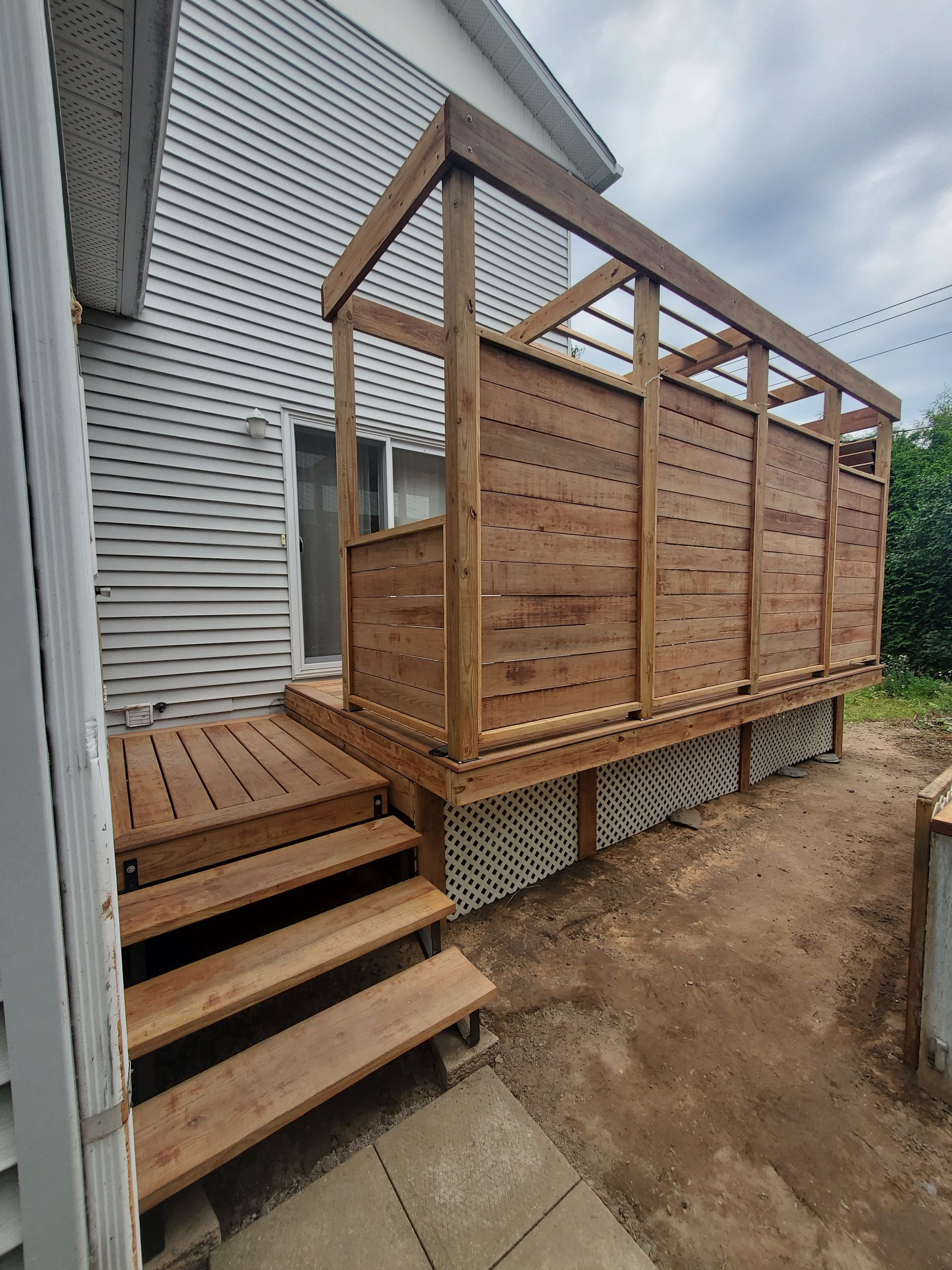 Une terrasse en bois avec des escaliers est en cours de construction sur le côté d'une maison.