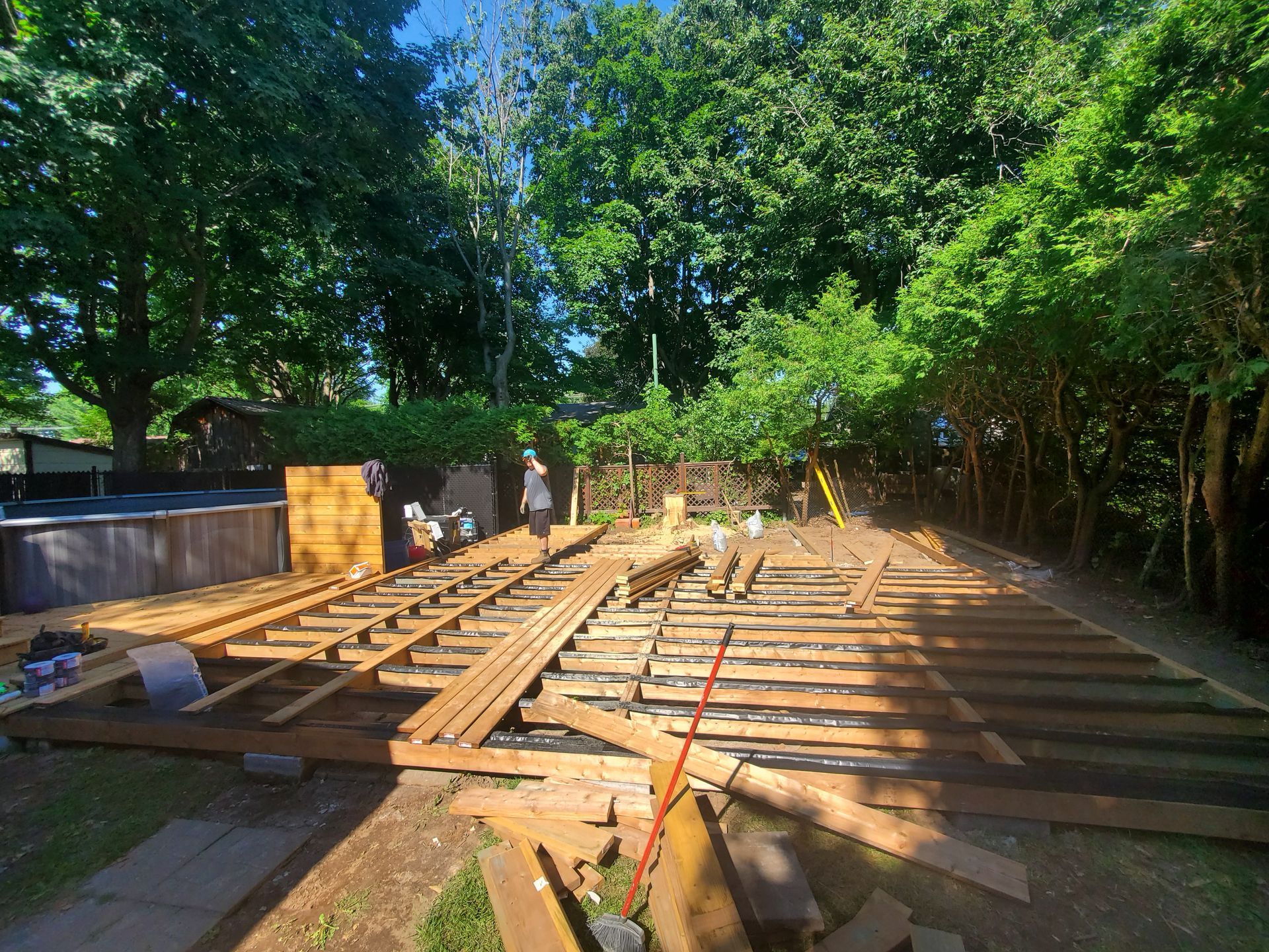 Une terrasse en bois est en cours de construction dans une cour arrière entourée d'arbres.