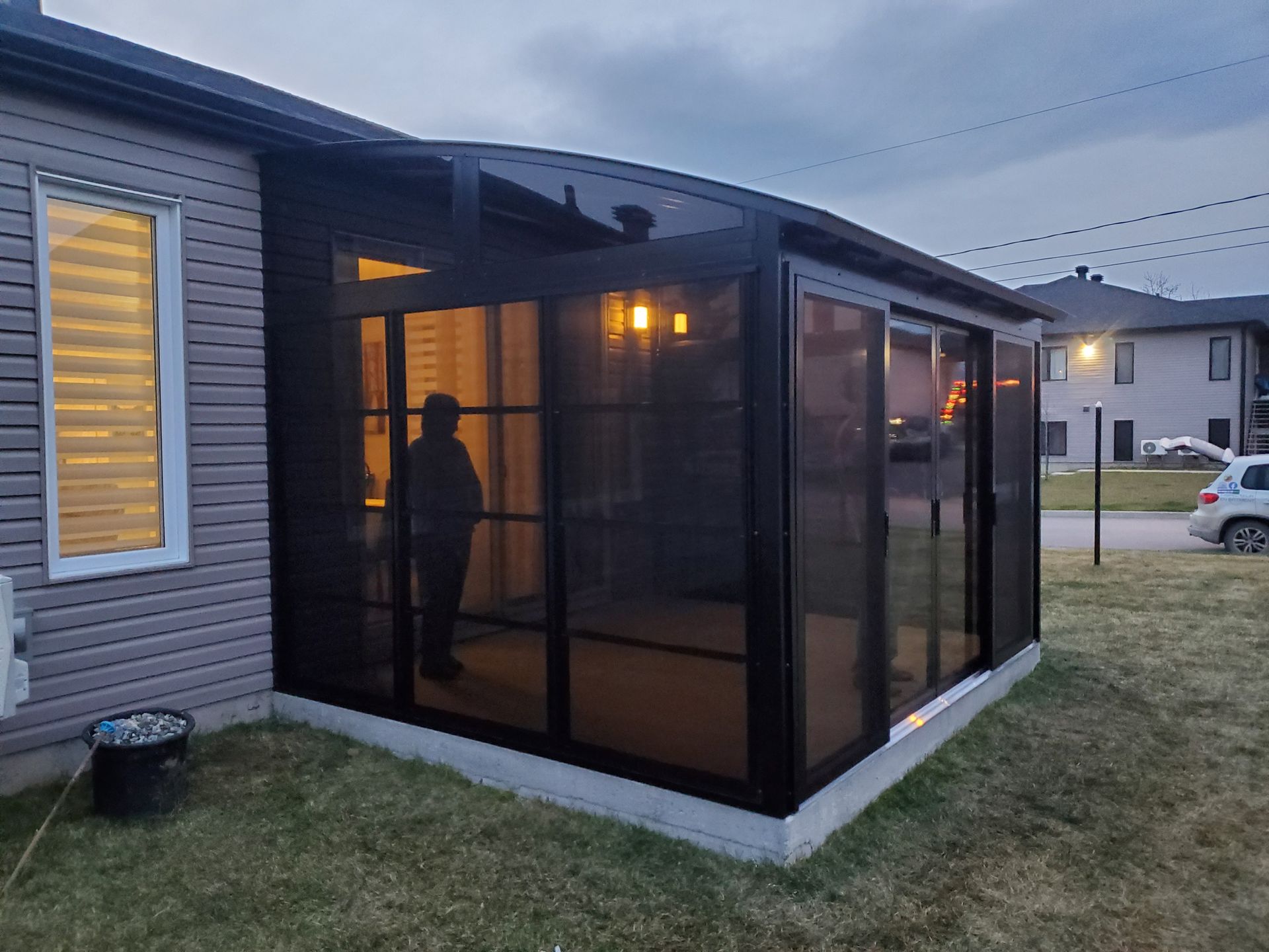 Un homme se tient debout sur un porche grillagé à côté d'une maison.