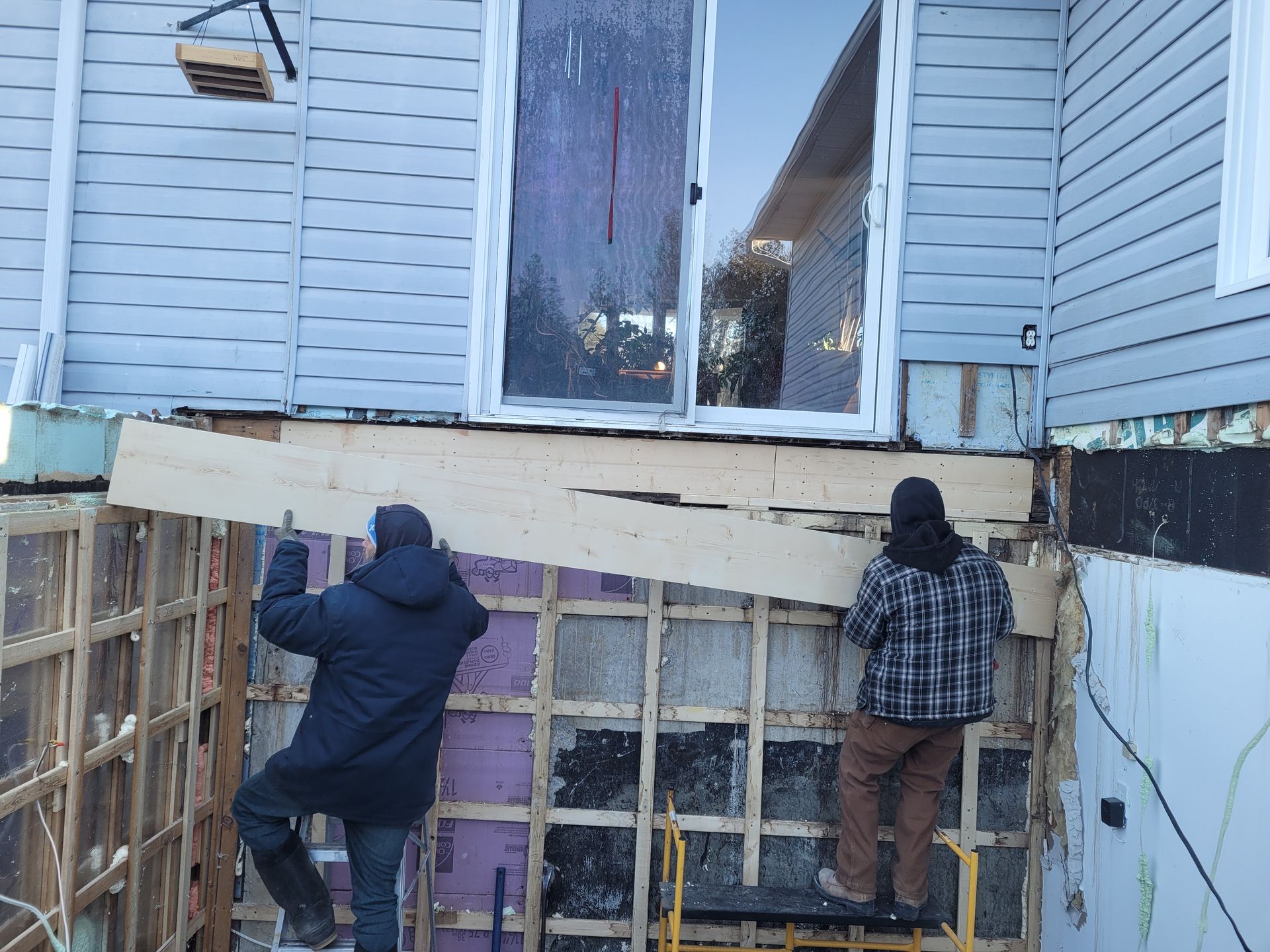 Deux hommes travaillent sur le côté d'une maison.