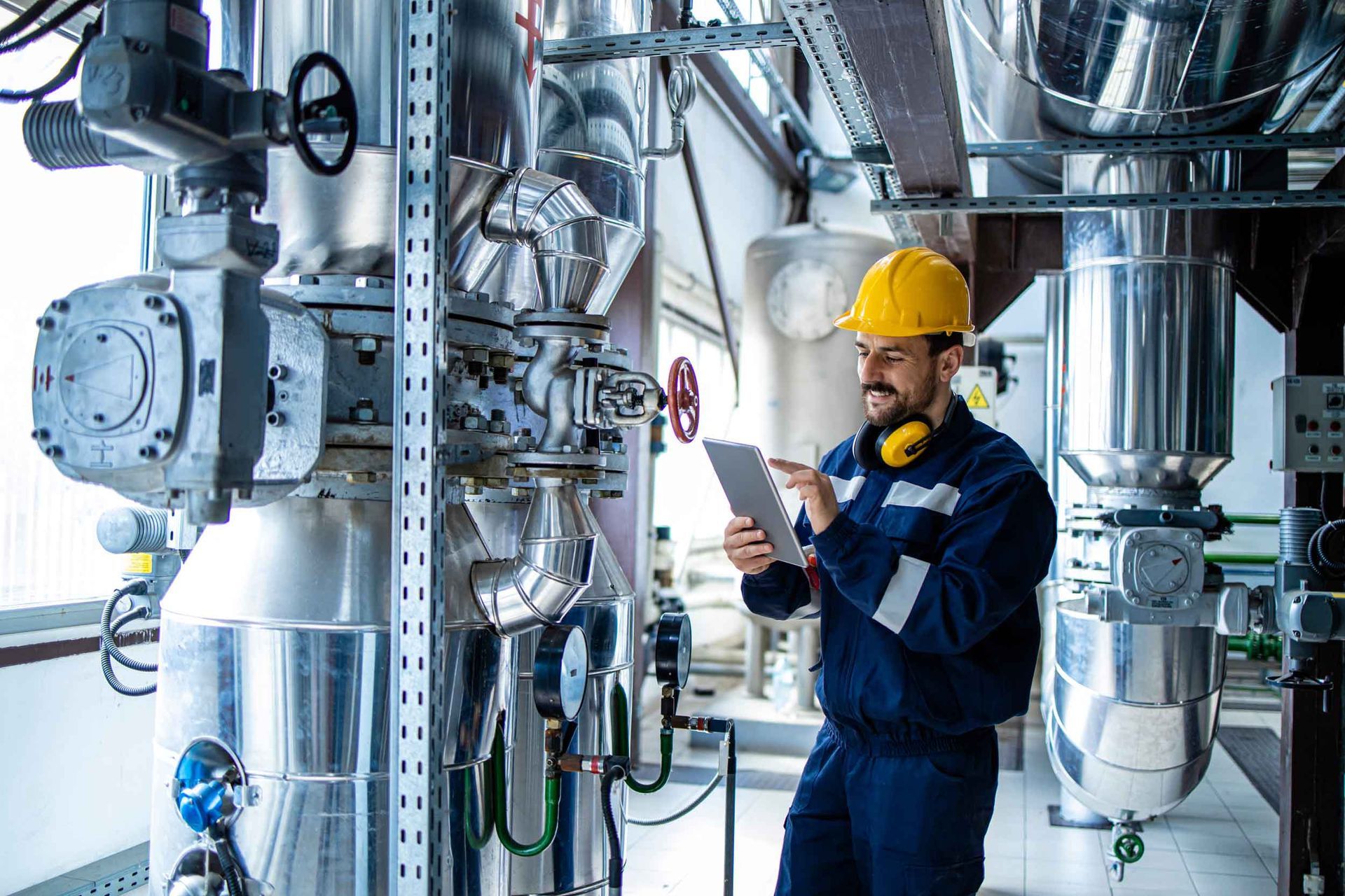 Heating plant interior with pipes and valves and a factory worker controlling the process of boiling.