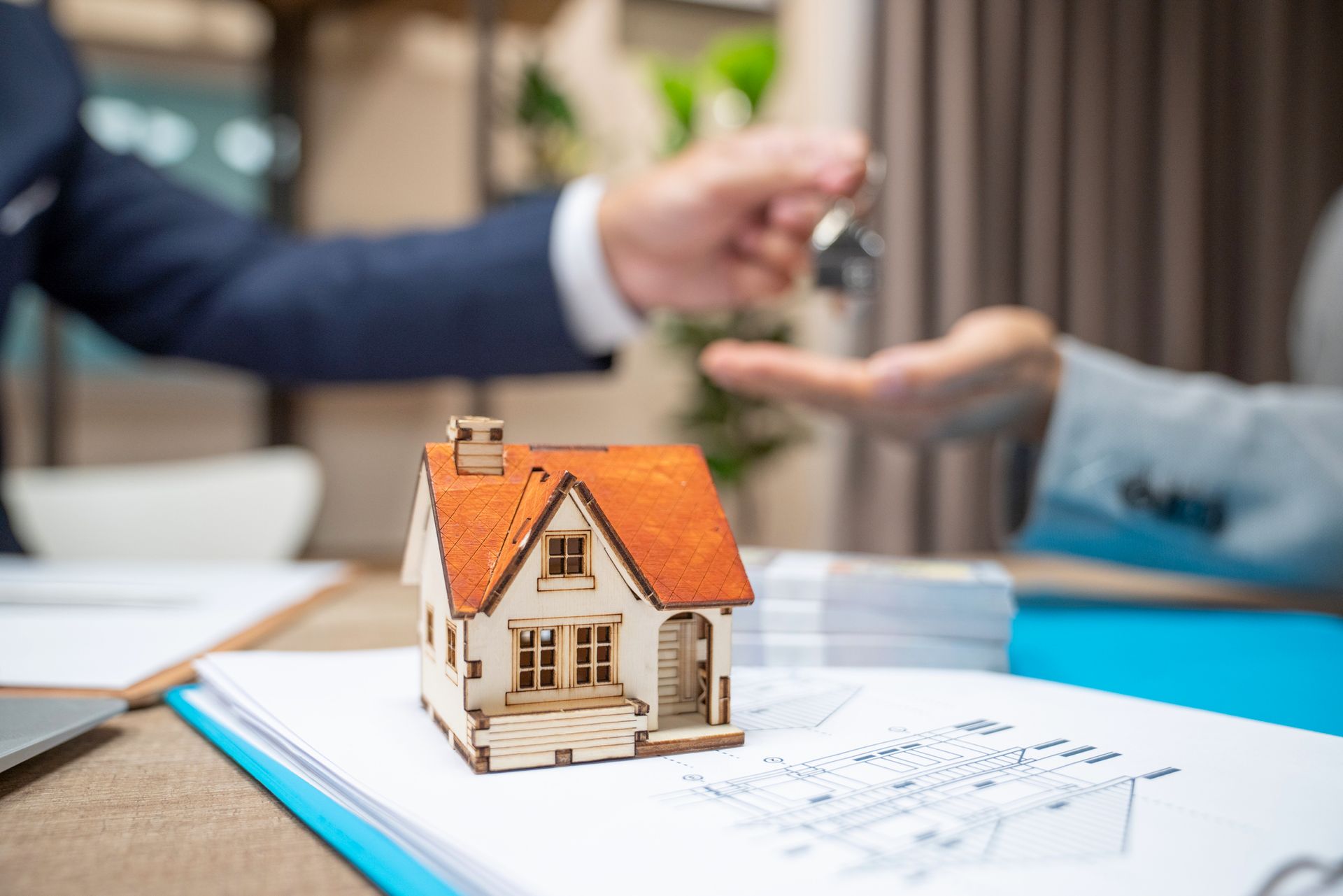 A man is handing a key to a woman next to a model house.