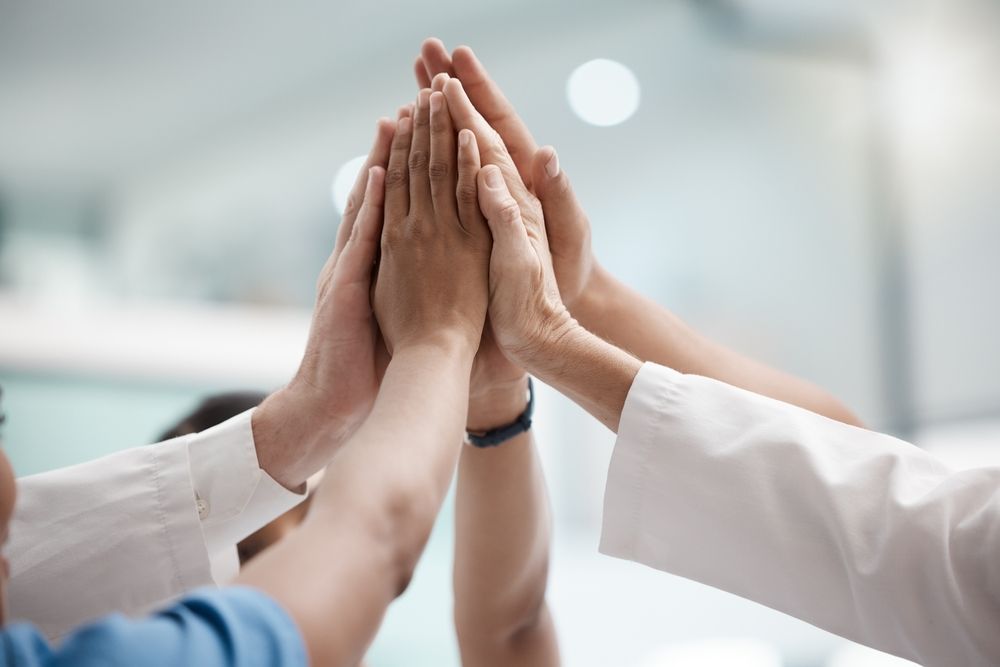 Hands of multiple people raised in a high-five, symbolizing teamwork and collaboration.