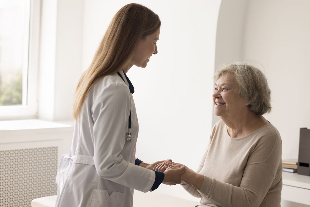 Doctor holding hands with an elderly patient in a bright medical office, both smiling.