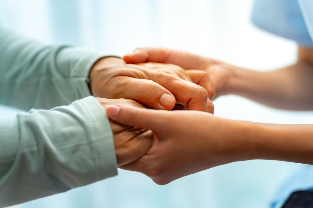 Hands of an elderly person held by a younger person, offering comfort and support.