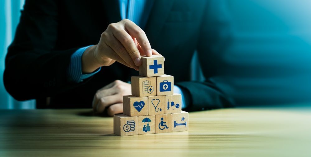 Person in suit building a pyramid of wooden blocks with health icons.