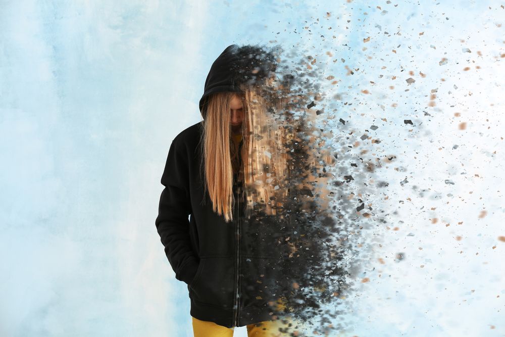 Woman in hoodie disintegrating into particles against a light blue backdrop.