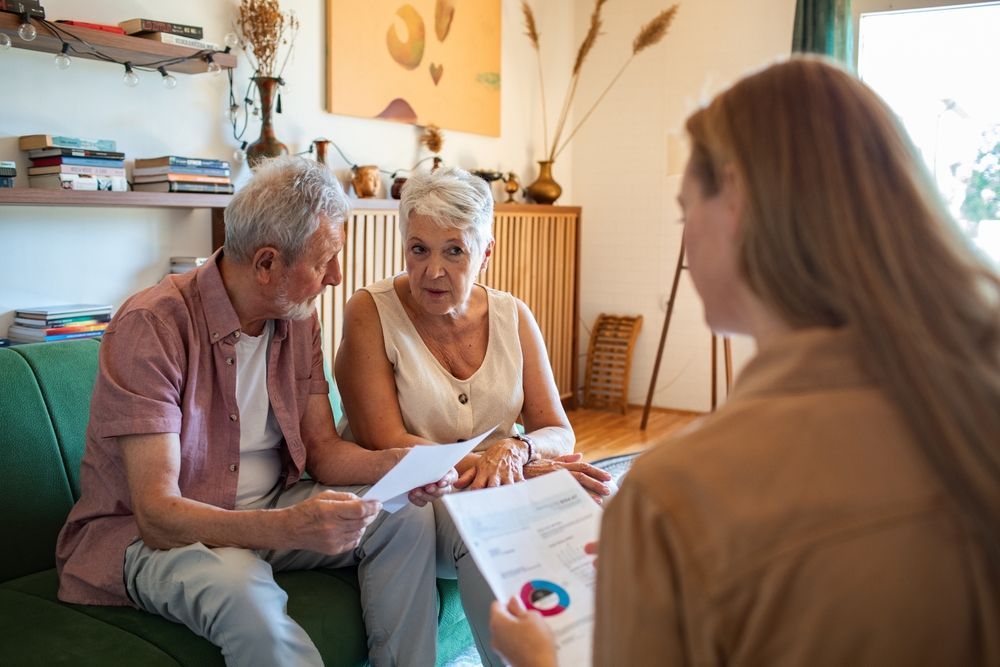 Older couple reviews documents with a young woman in a living room; discussing finances.