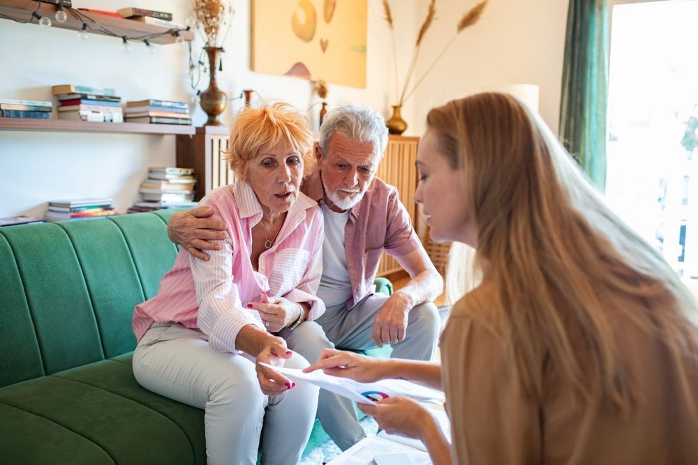 Woman shows document to concerned elderly couple on a green couch.