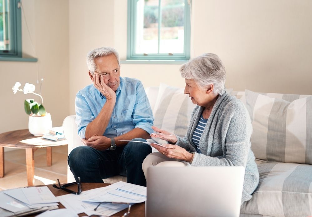 Senior couple reviewing papers on a sofa, discussing finances in a living room.