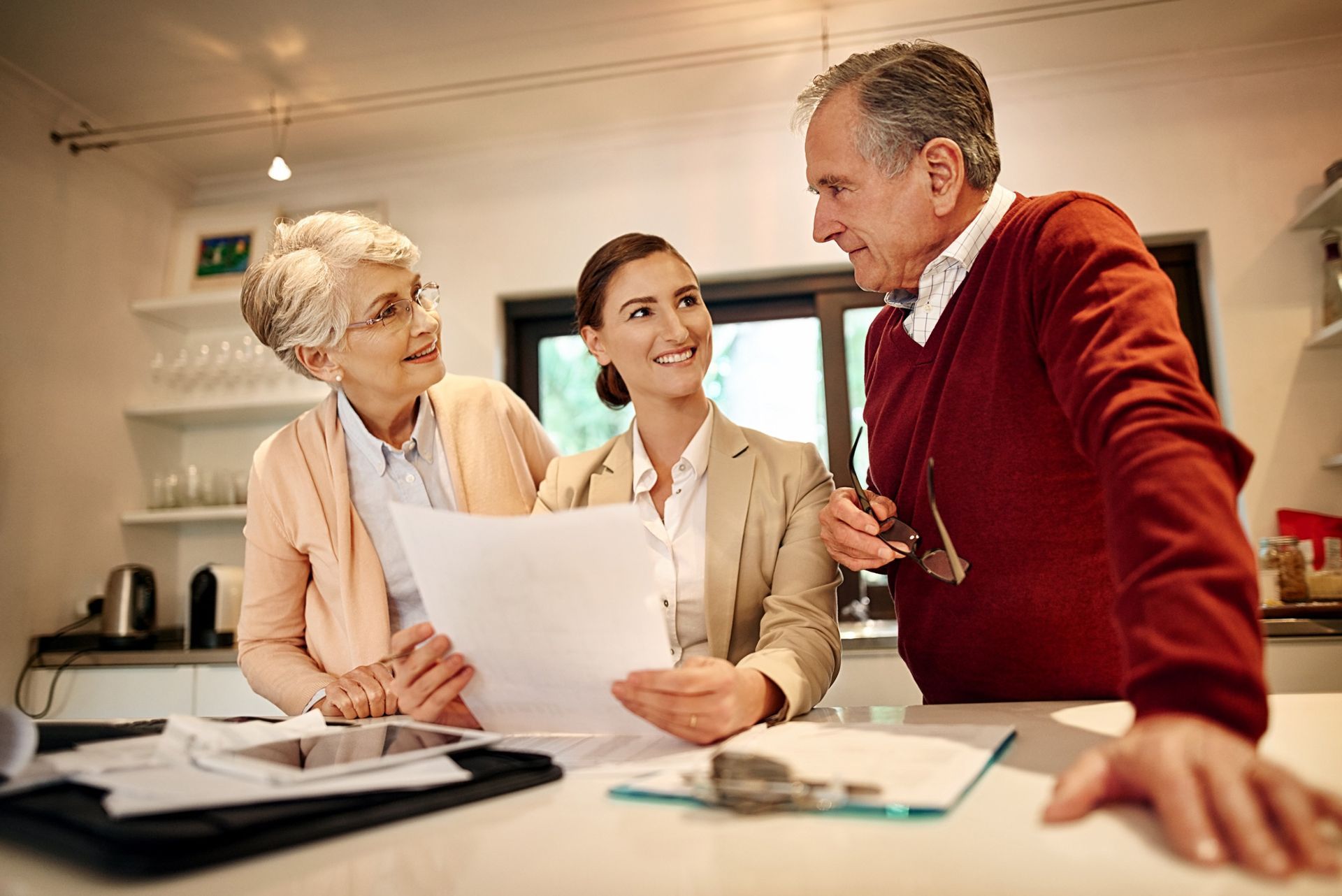 Financial advisor shows documents to senior couple in a kitchen.