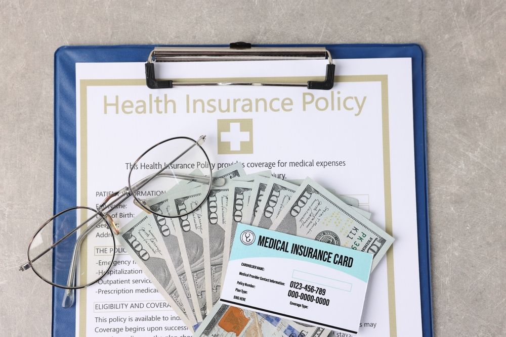 Health insurance policy document, cash, and glasses on a clipboard. Medical card is visible.