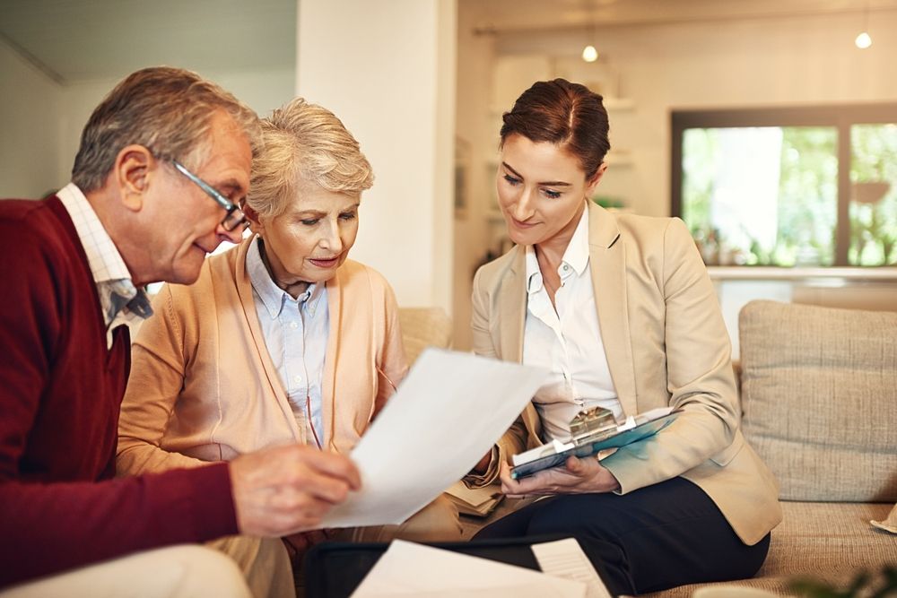 Senior couple reviews documents with a financial advisor on a living room couch.