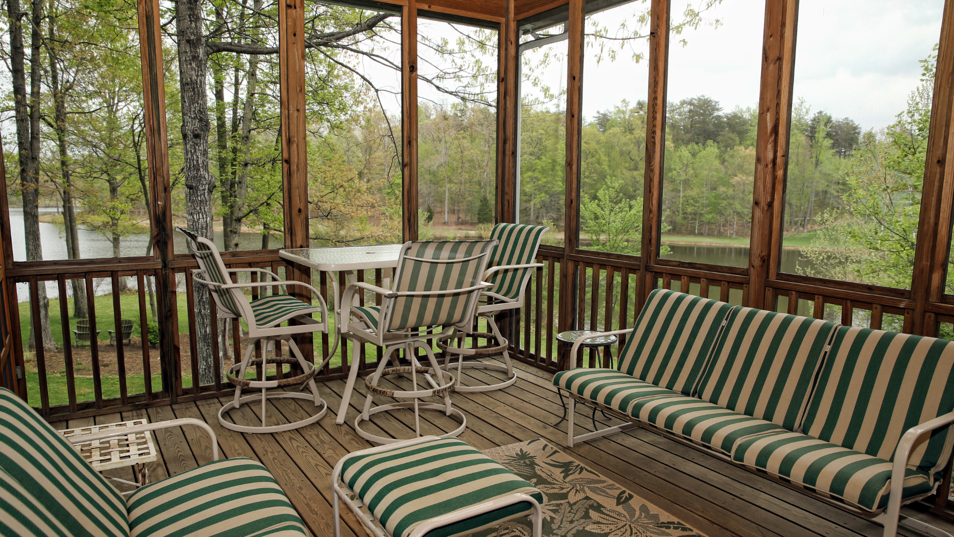 A screened in porch with a couch , chairs , table and ottoman.