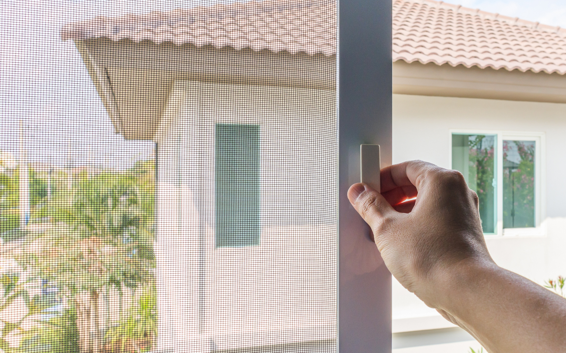A person is opening a screen door to a house.