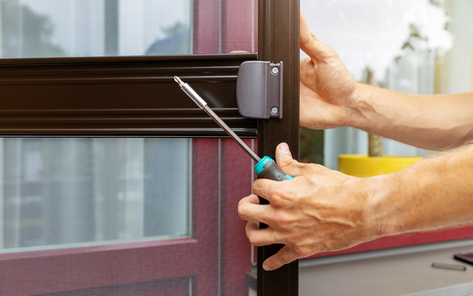 A person is fixing a screen door with a screwdriver.