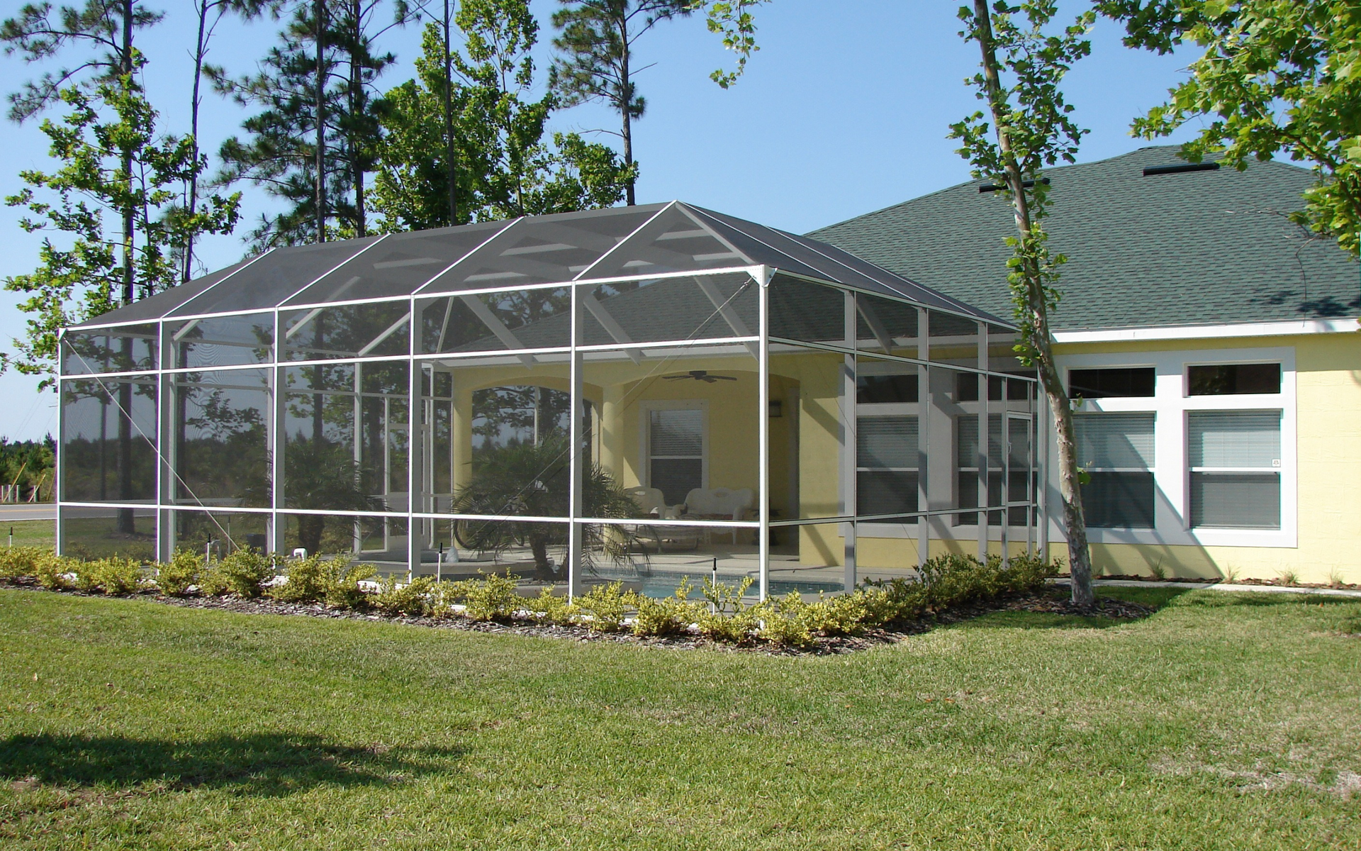 A yellow house with a screened in porch and a green roof