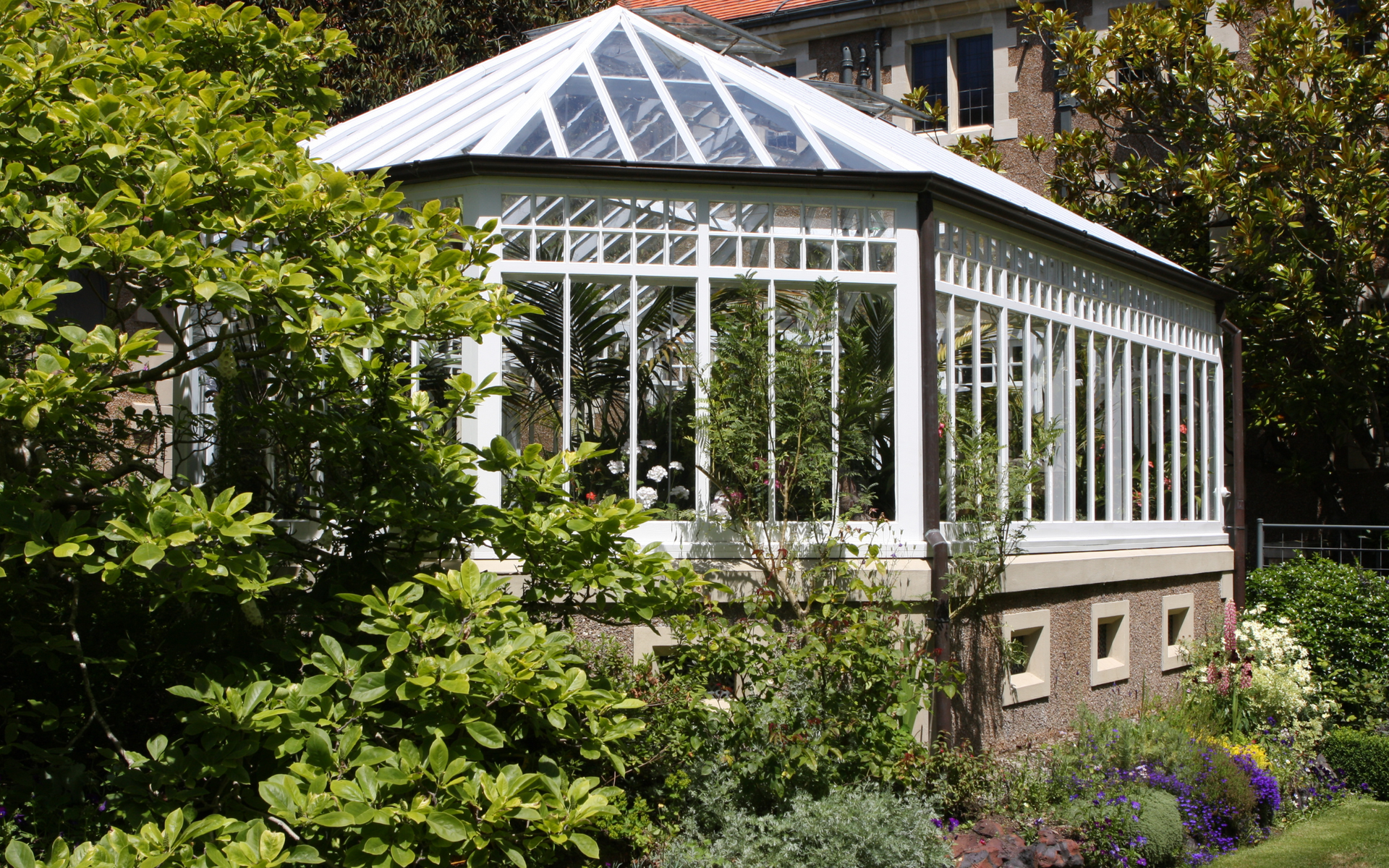 A greenhouse is surrounded by trees and flowers in a garden.