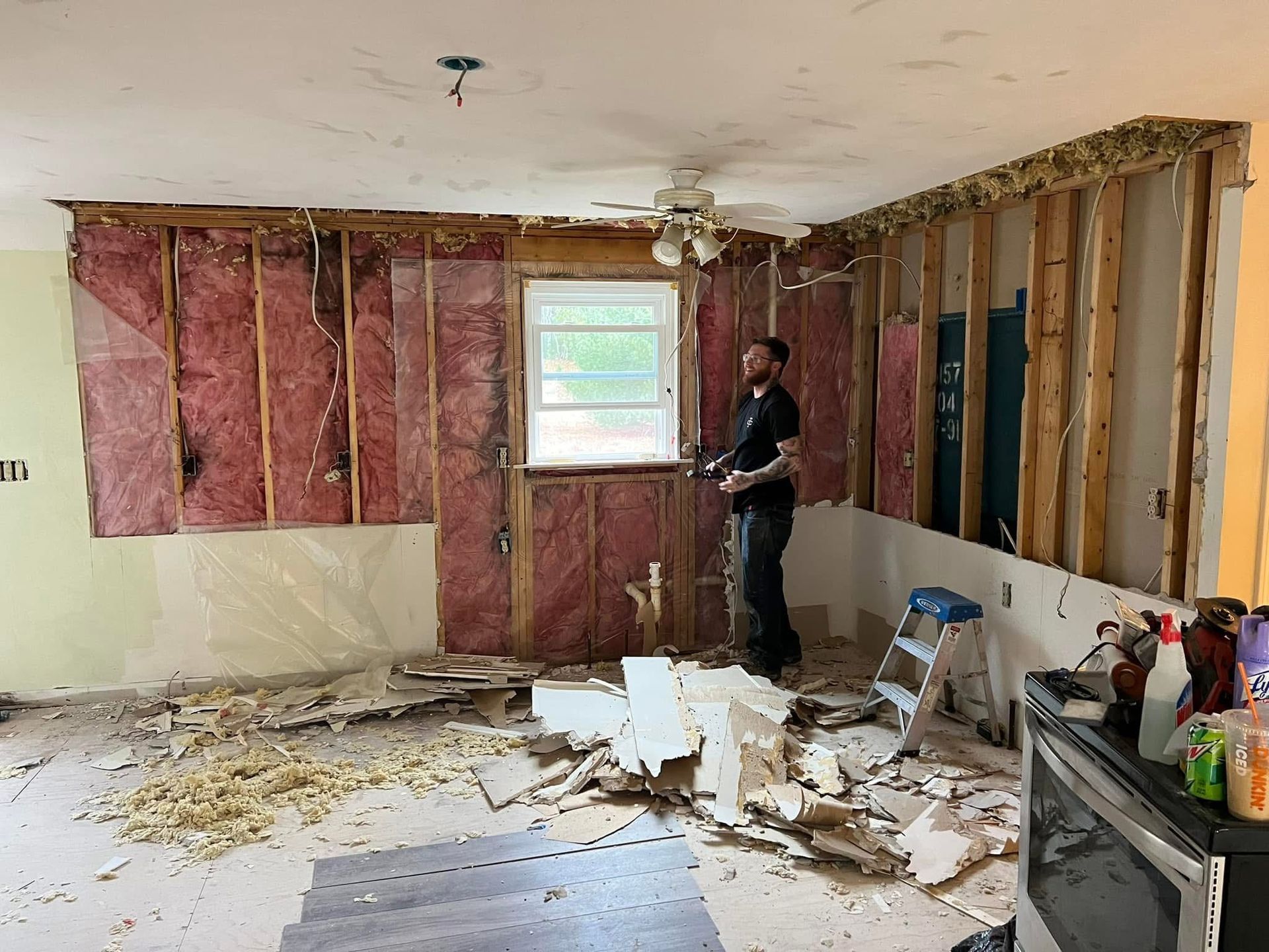 Room demolition: Man standing amidst debris, exposed wall studs, pink insulation.