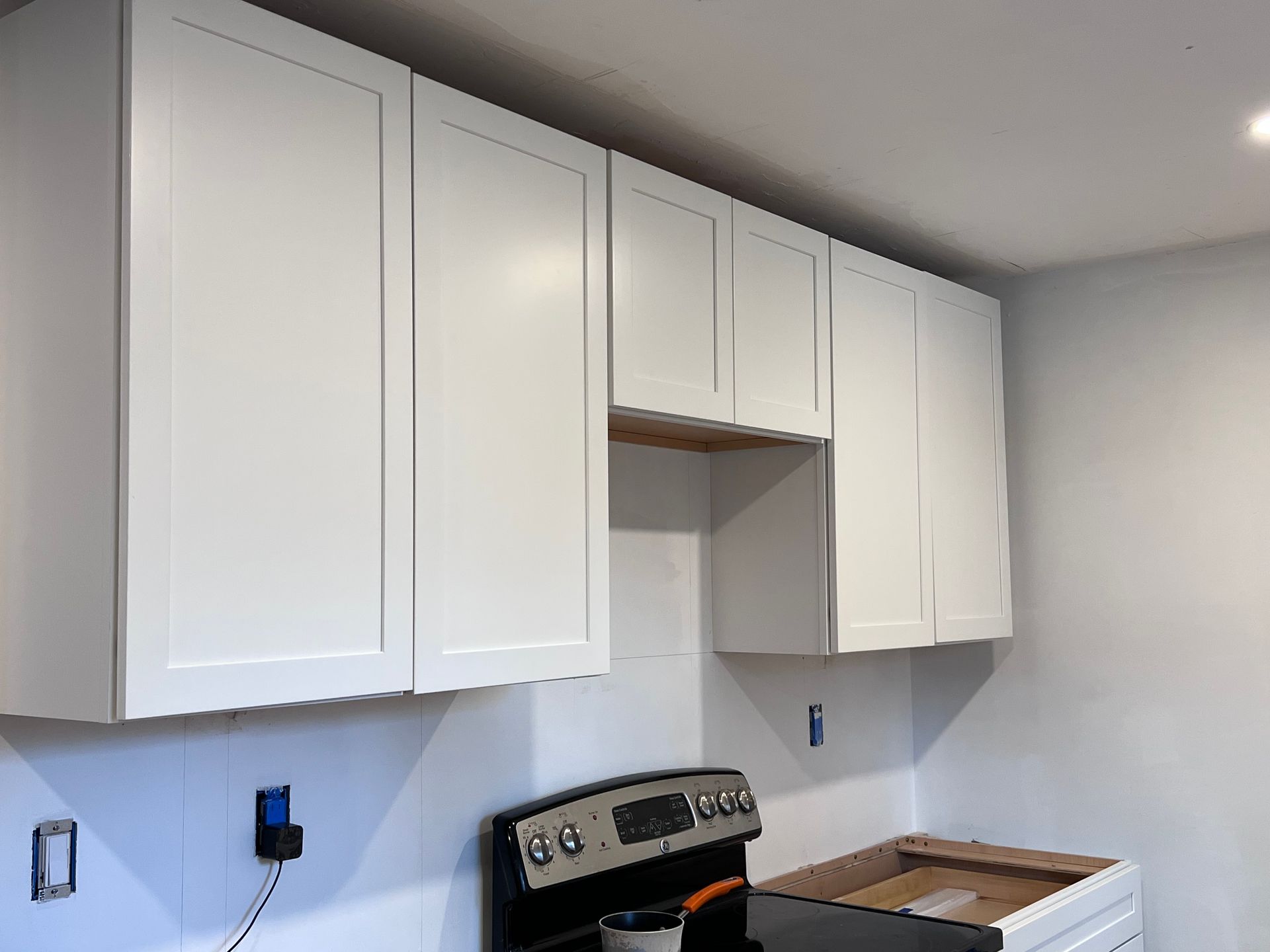 White kitchen cabinets installed above a stove and unfinished base cabinets.