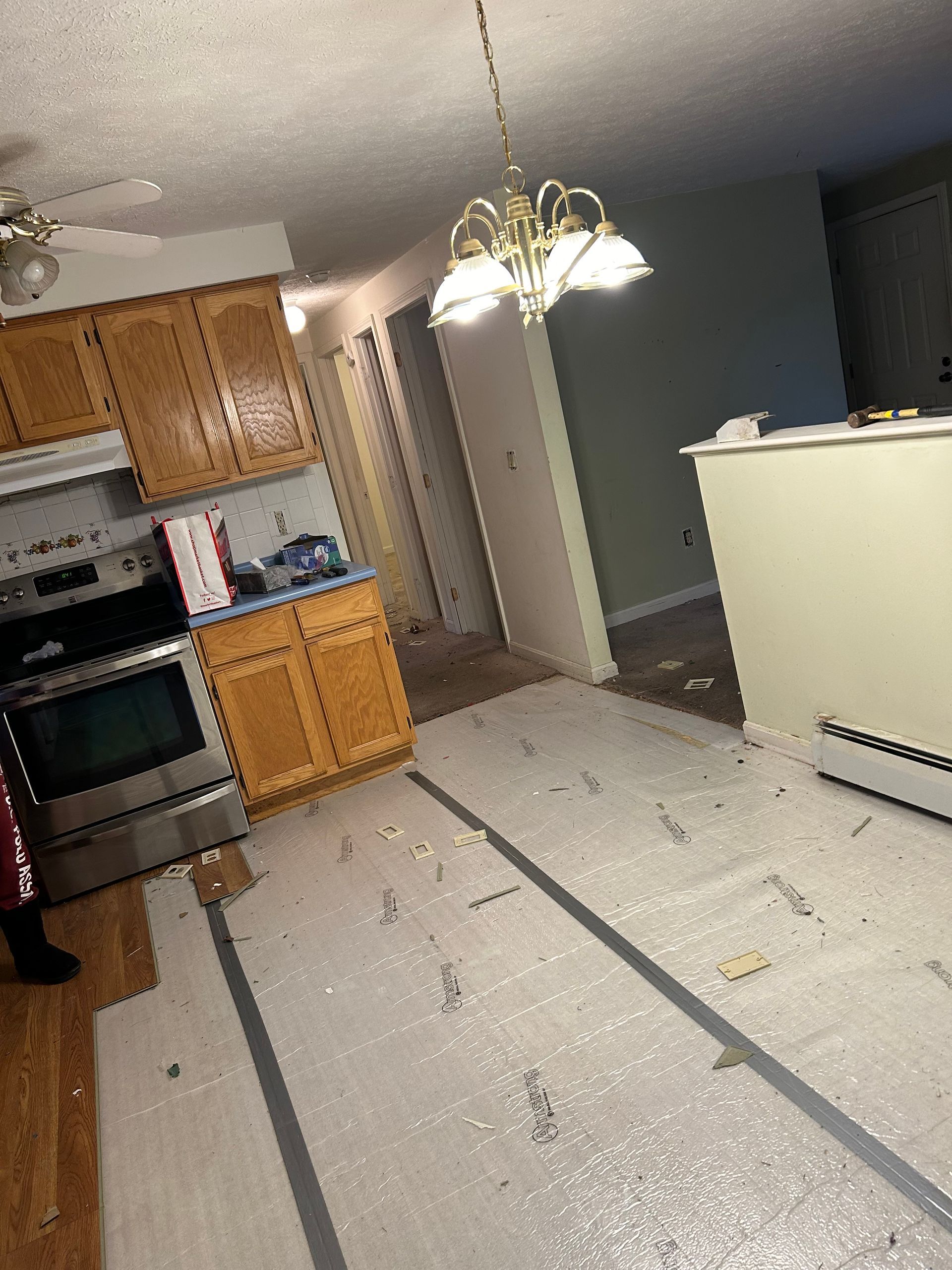 Kitchen renovation: Cabinets, appliances, bubble wrap on floor, debris, and a light fixture.
