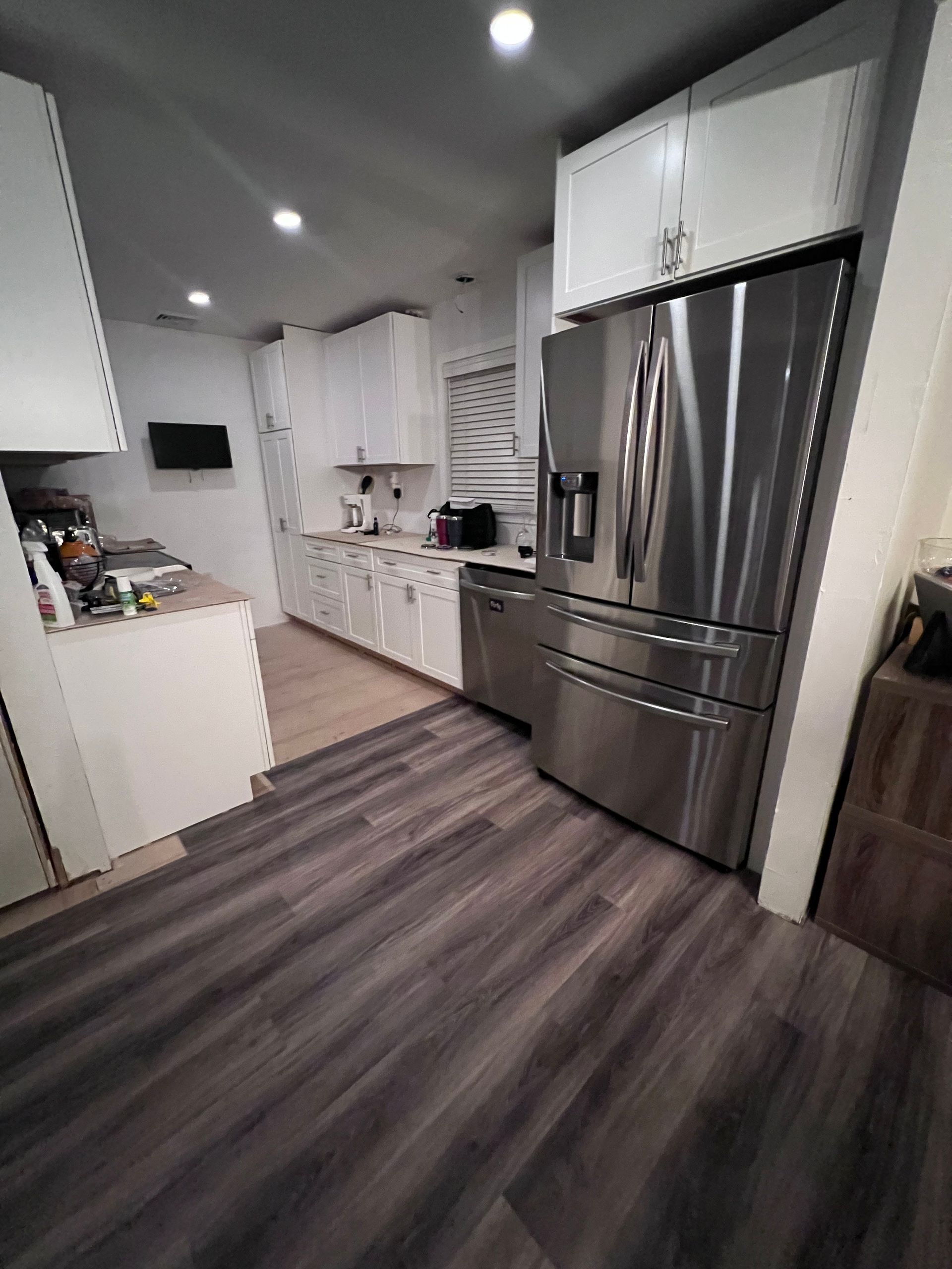 Modern kitchen with white cabinets, stainless steel appliances, and dark wood-look flooring.