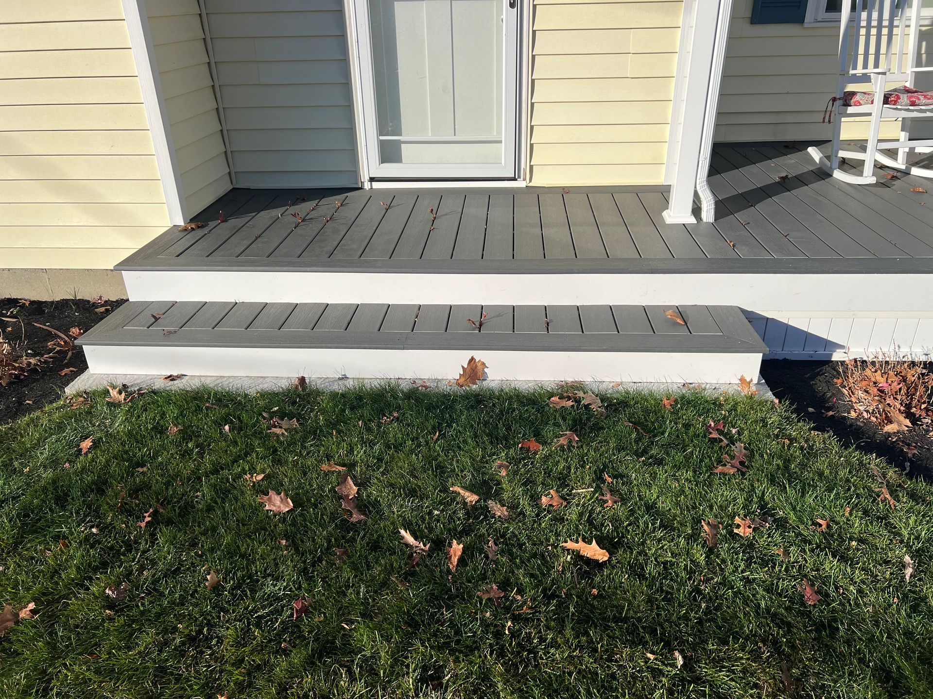 A house entrance with a gray deck and stairs leading to a door, over green grass.