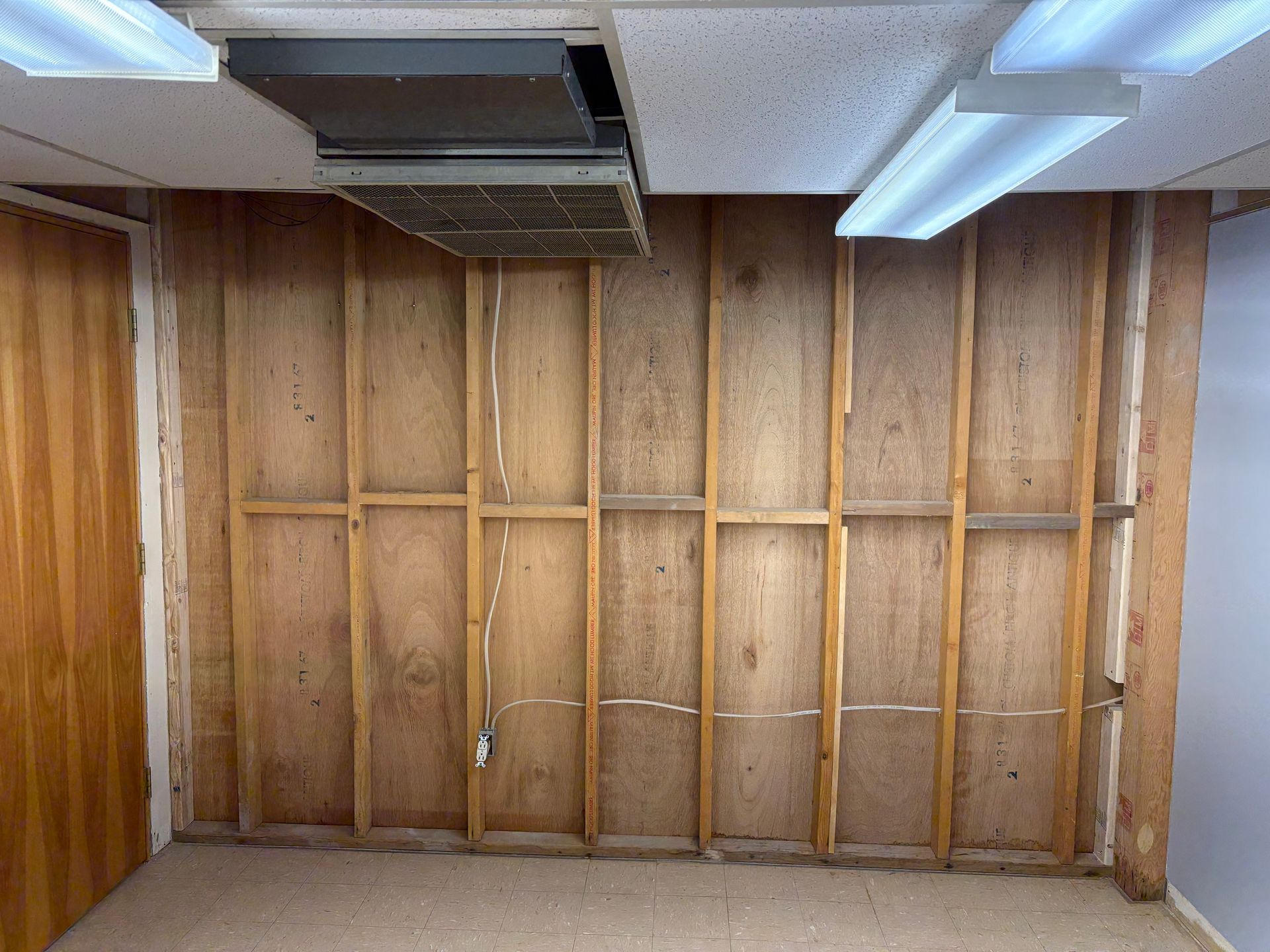 Interior wall with exposed wooden studs, missing paneling. Ceiling lights and vent visible.