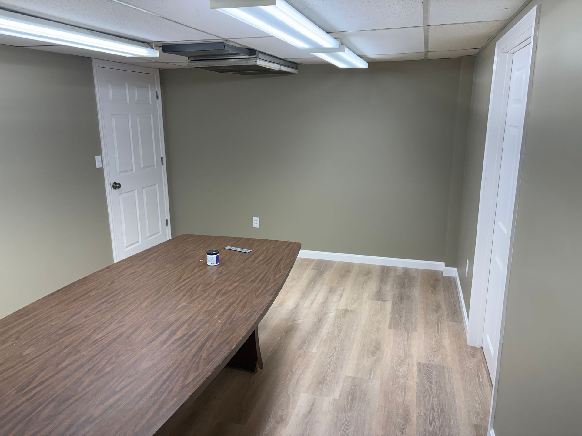 Empty room with long wooden table, two white doors, tan walls, and light-colored flooring.