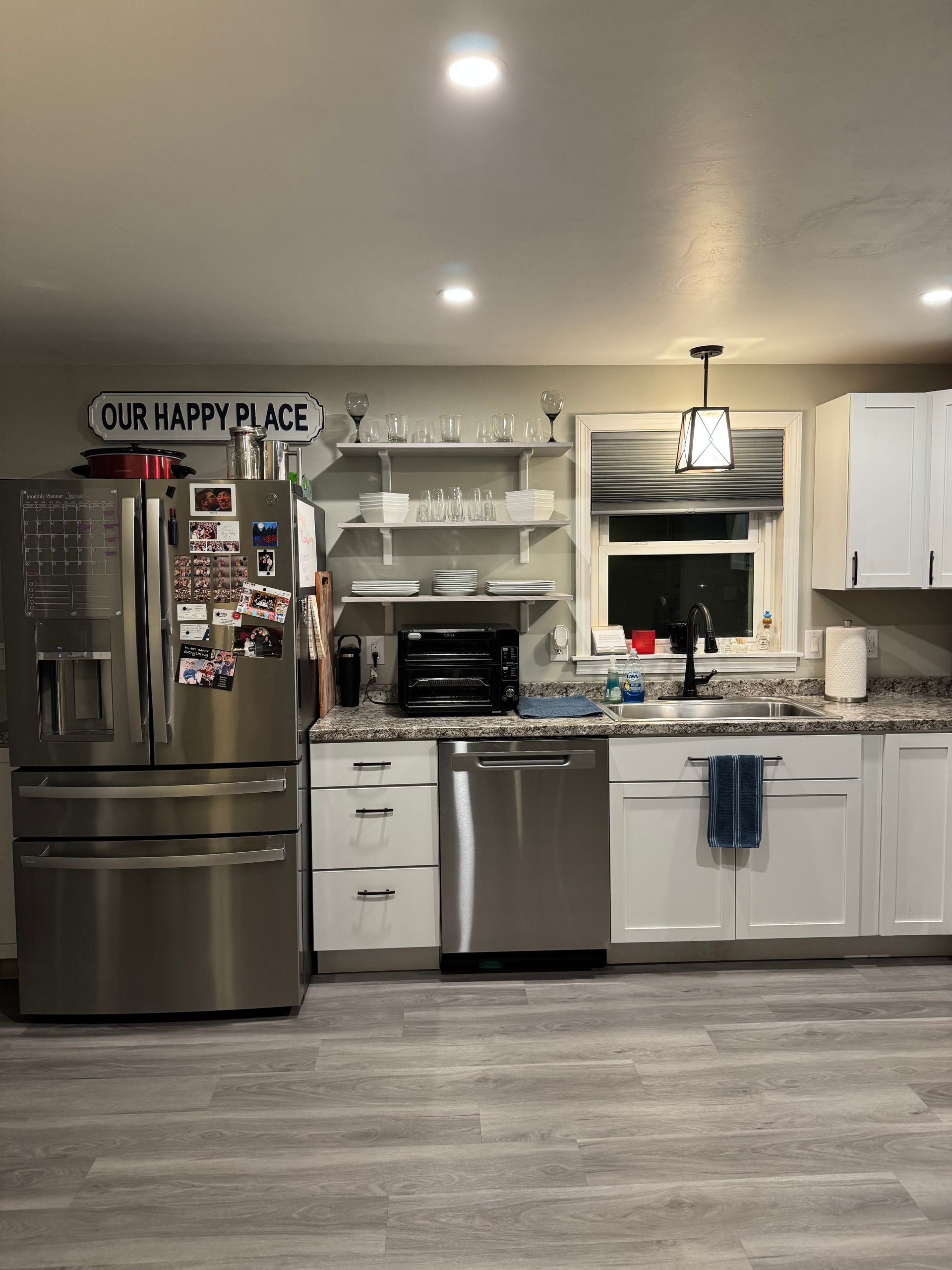 Stainless steel kitchen with white cabinets, appliances, and a window. Gray wood-look flooring.