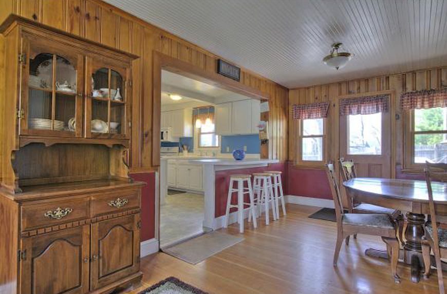 Dining room with wooden walls, hutch, round table, and a partial view of the kitchen.