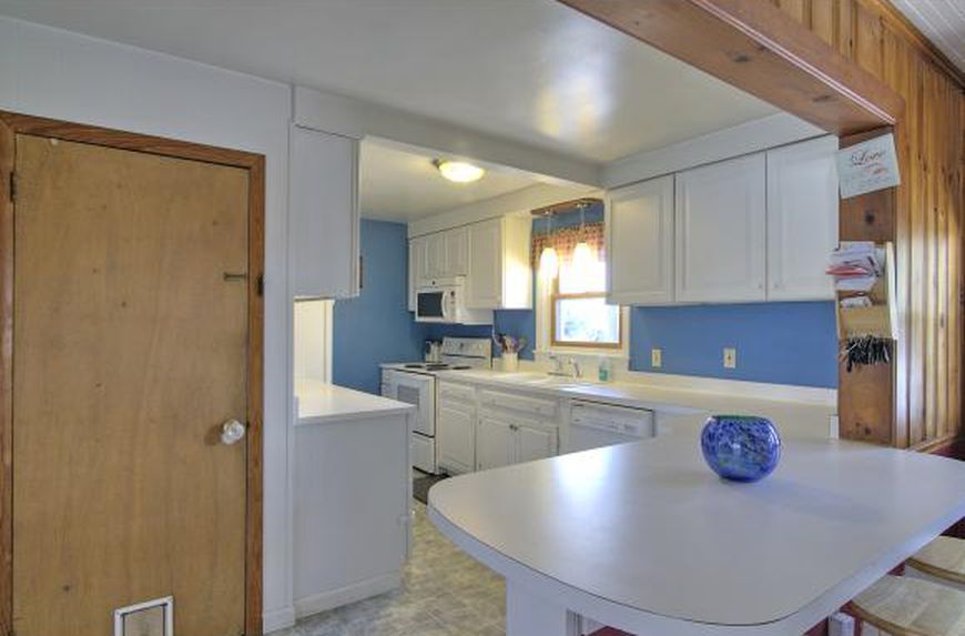 Bright kitchen with white cabinets, blue backsplash, and light wood door.