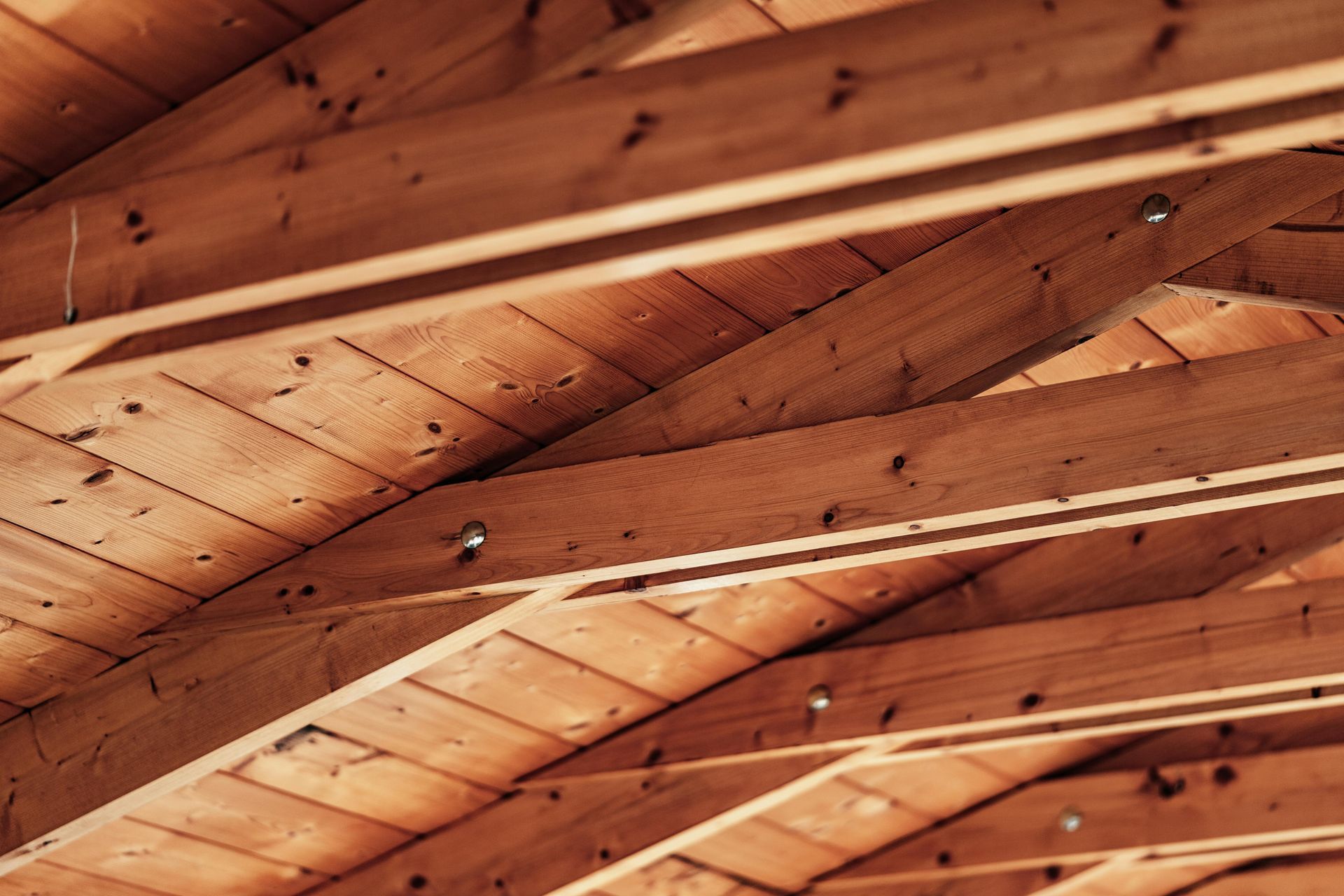 Wooden rafters in a roof, visible from below. Brown planks, sunlight and shadows.