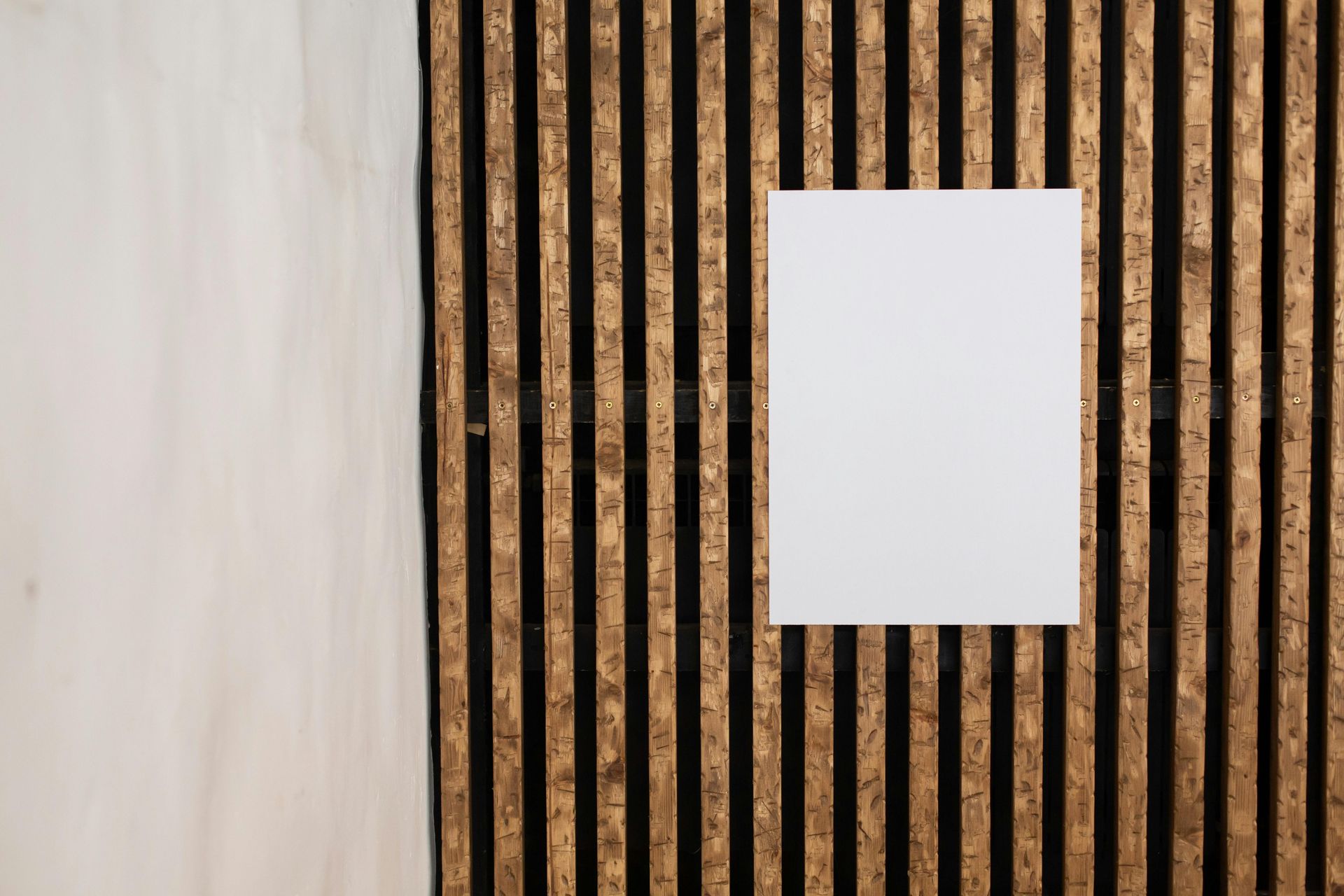 White poster on vertical wooden slats, next to a white wall.