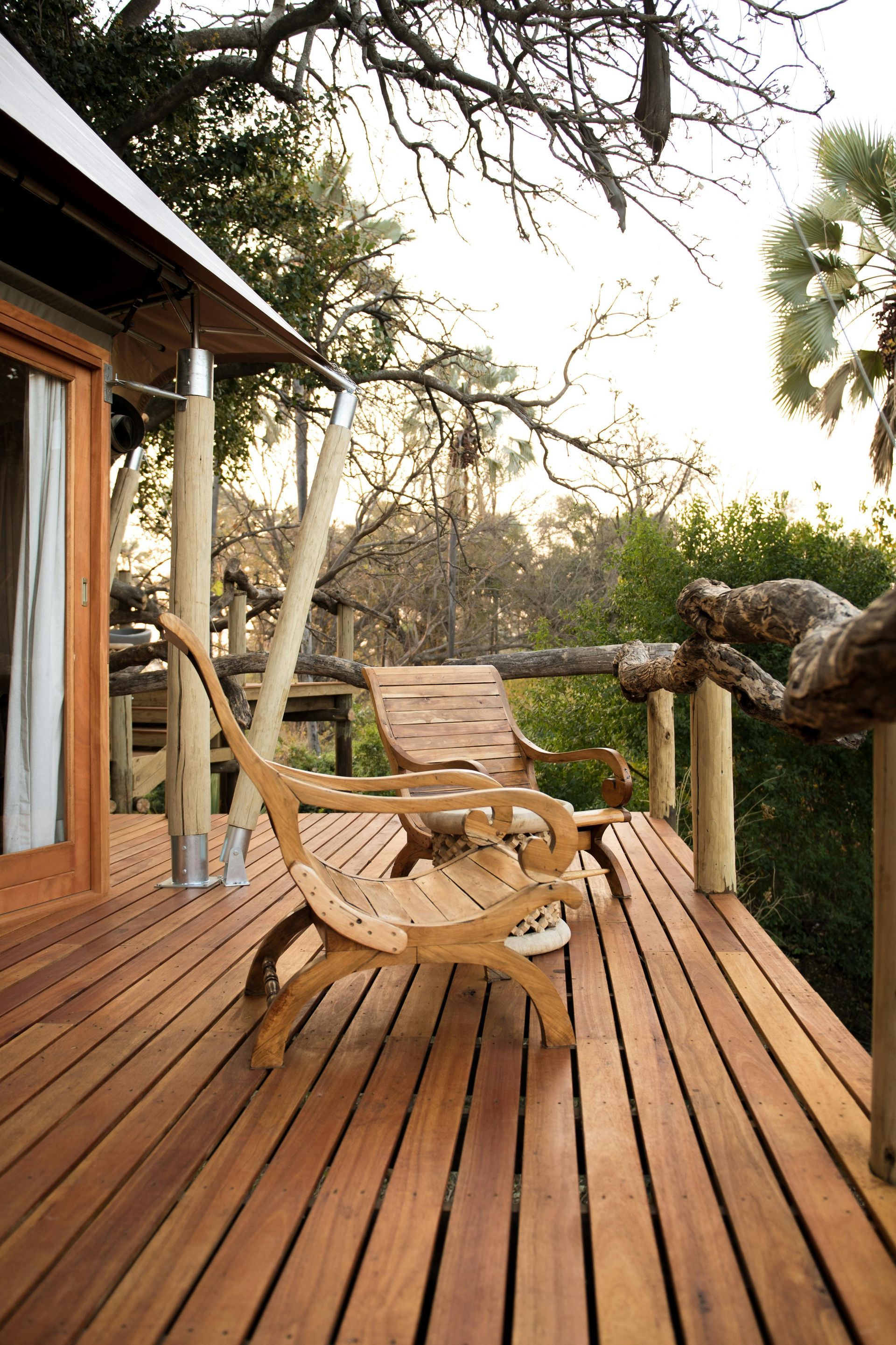 Wooden deck with two chairs, overlooking a tree-filled landscape. Bright sunlight.